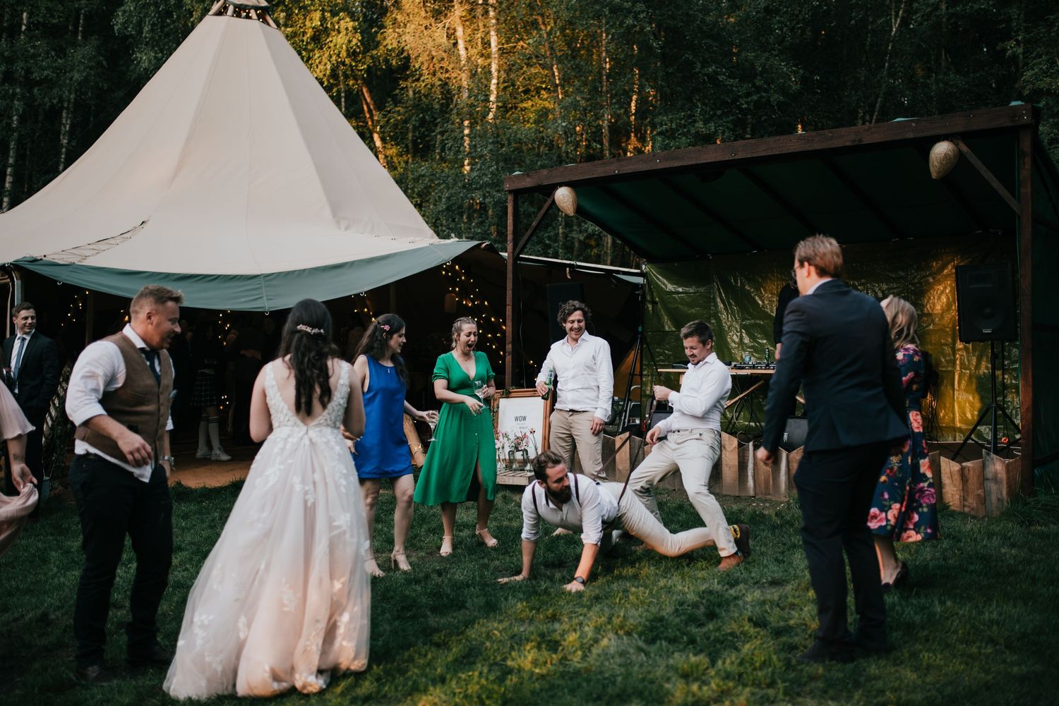 Wedding guests dancing and celebrating on a grassy lawn with teepee tents in the background.