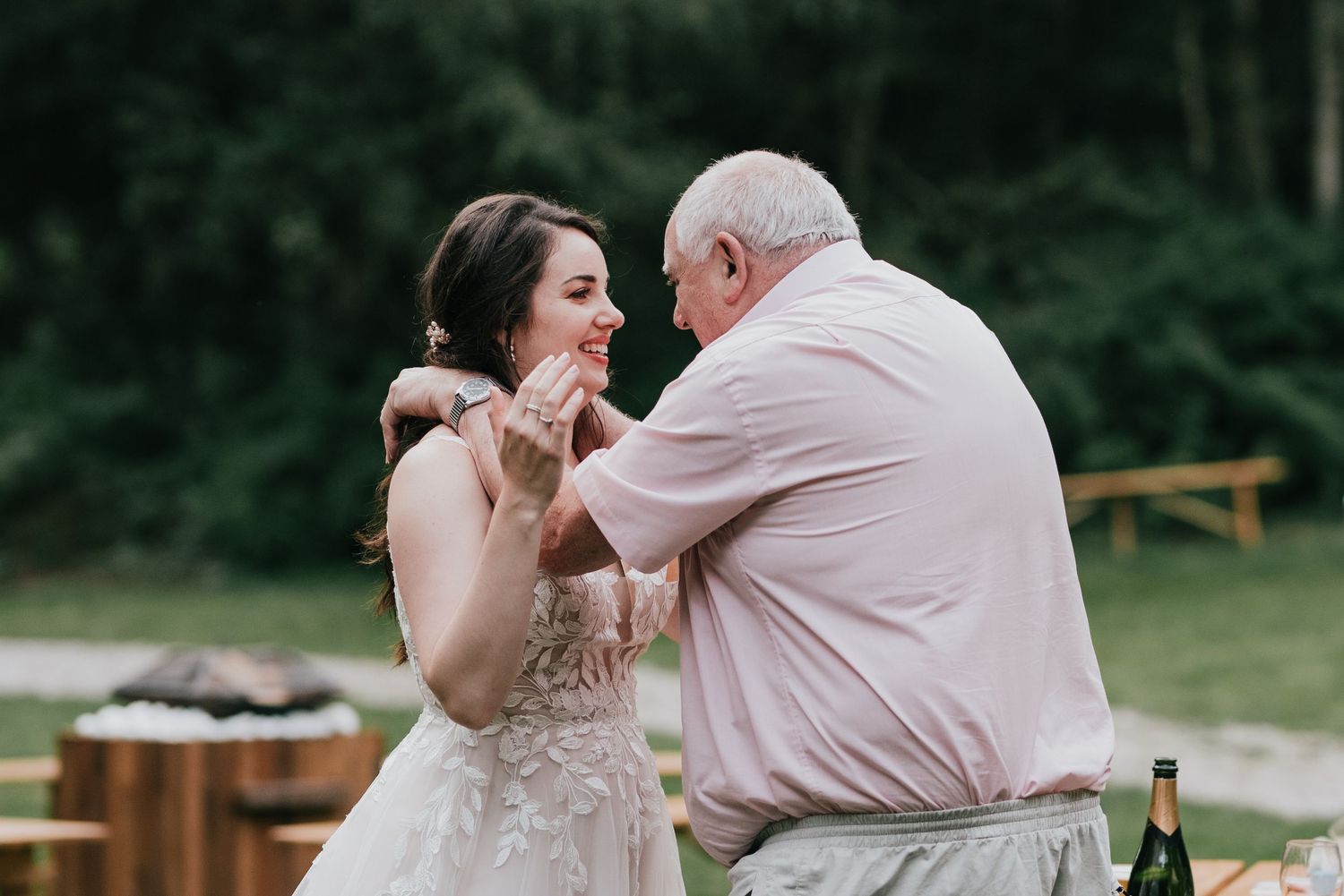 Emotional dance between a person in a lace wedding dress and another in pink at an outdoor reception.