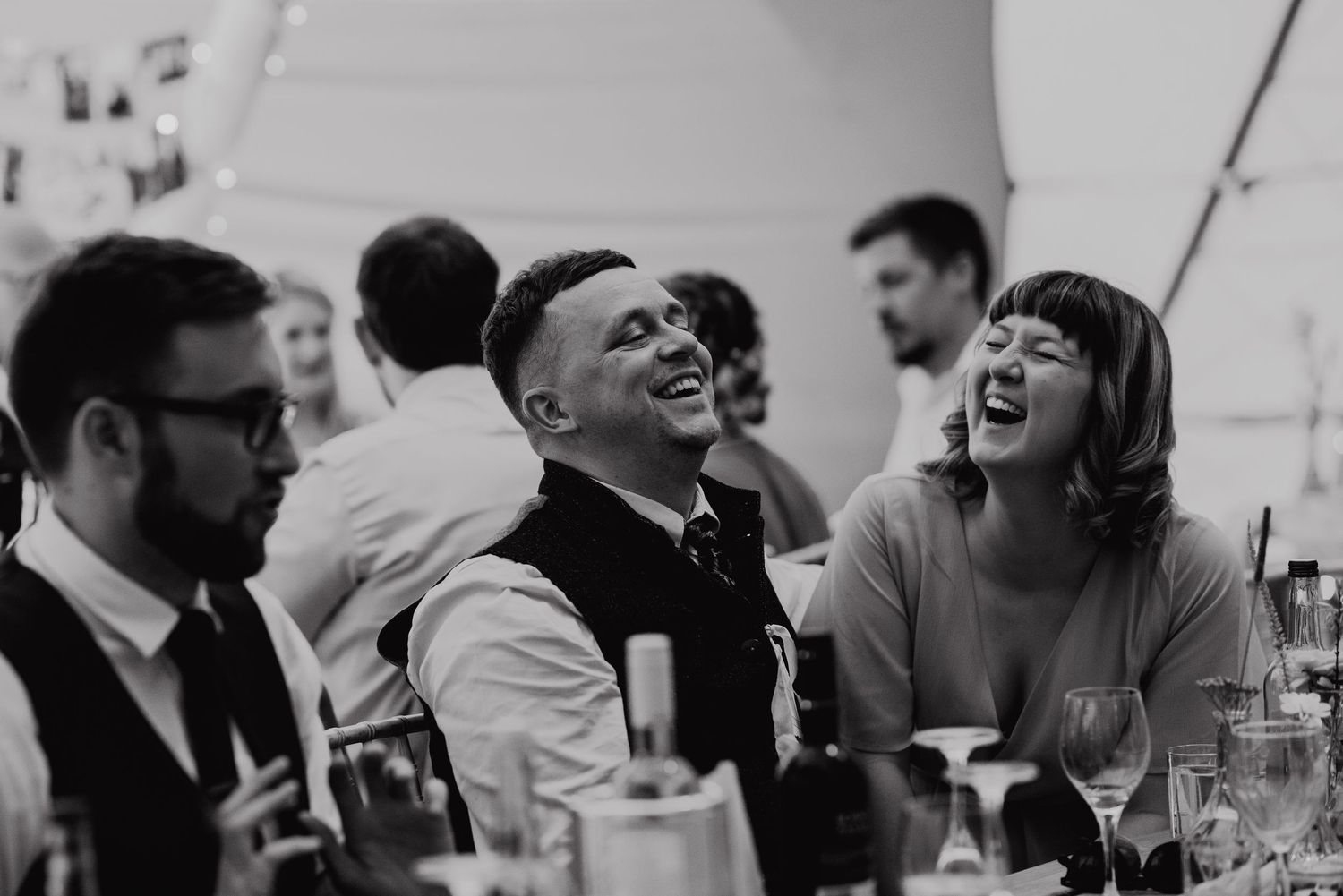Black and white photo of guests laughing heartily during wedding reception.