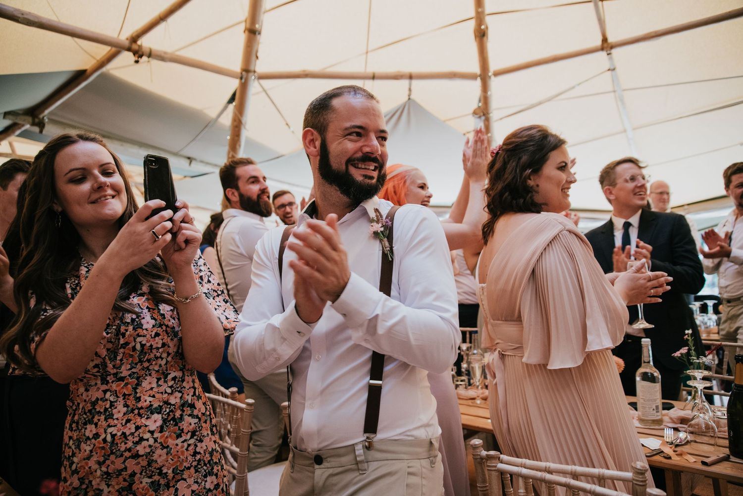 Wedding guests dancing and clapping during reception celebrations under a tent.