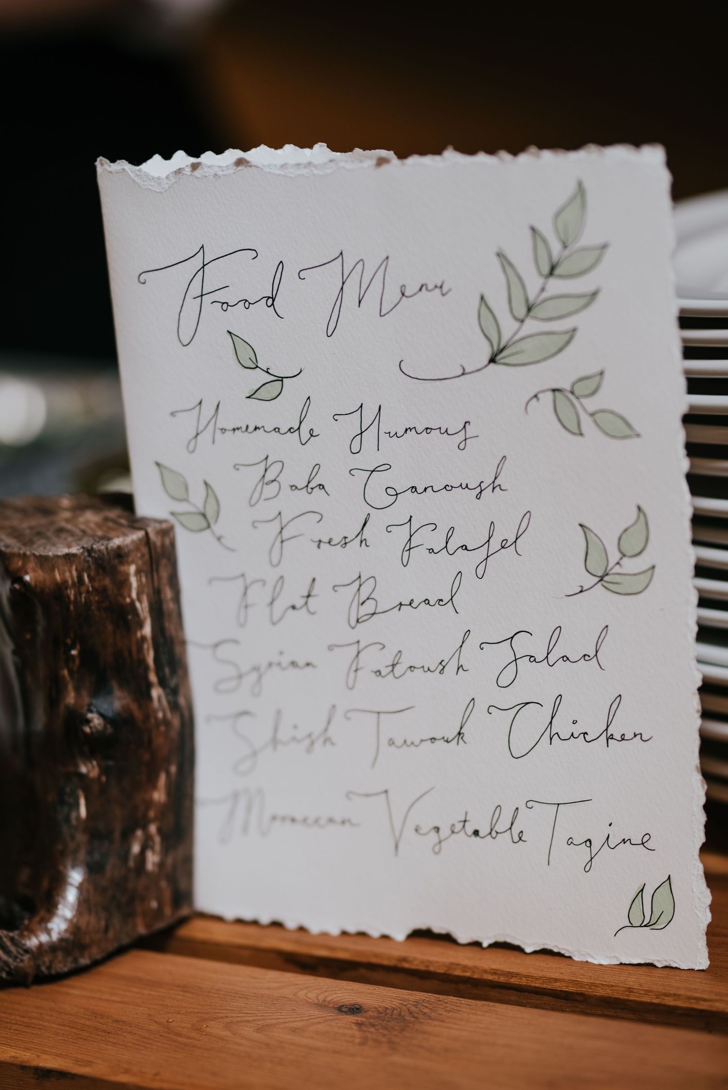 A rustic wedding menu card with delicate green leaf illustrations and handwritten text on torn-edge paper.