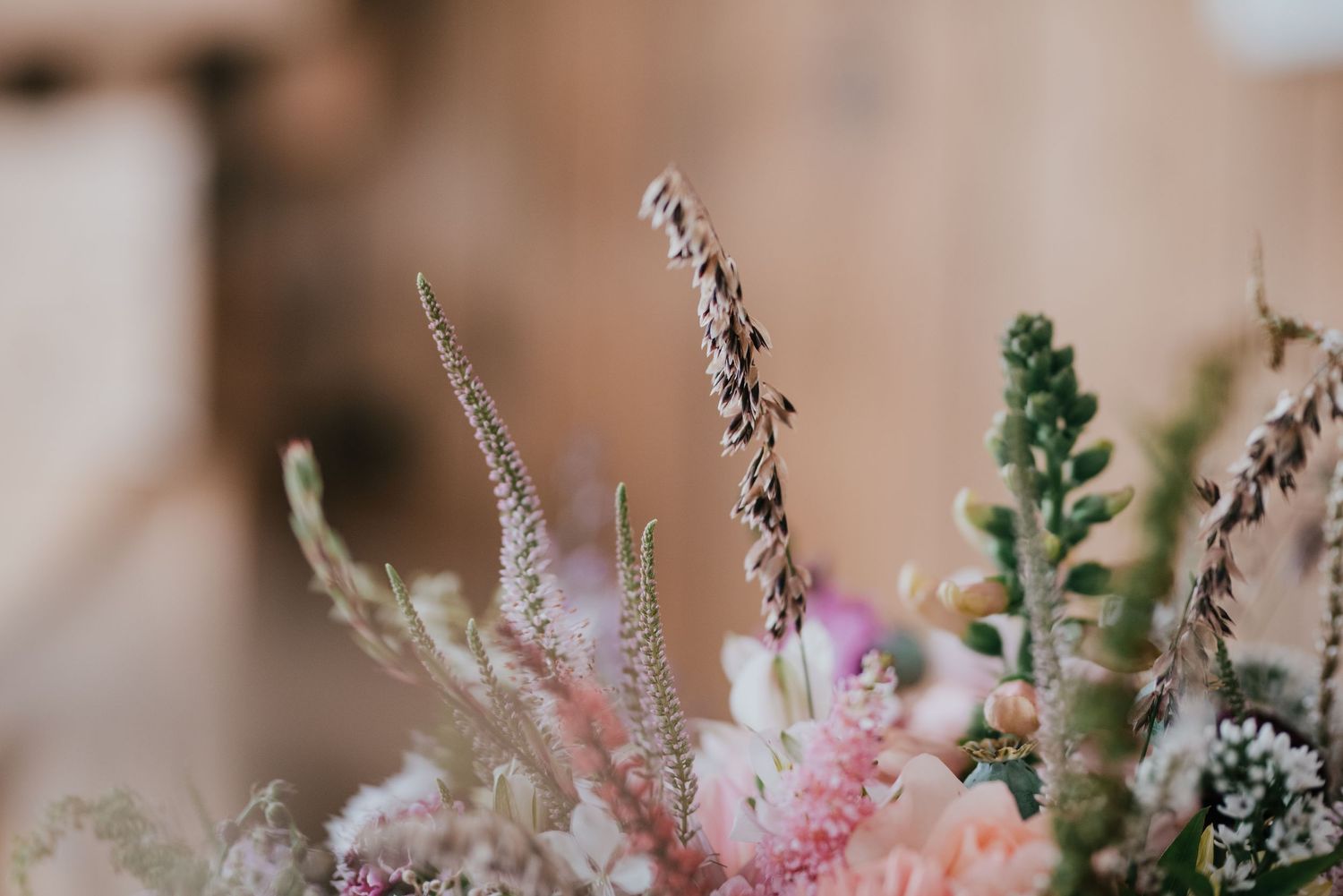 Close-up of delicate pink and white wildflowers and dried grass stems in a wedding bouquet arrangement.