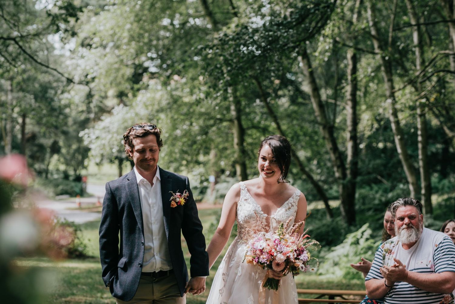 A couple walks together in a lush outdoor garden setting during a wedding ceremony.