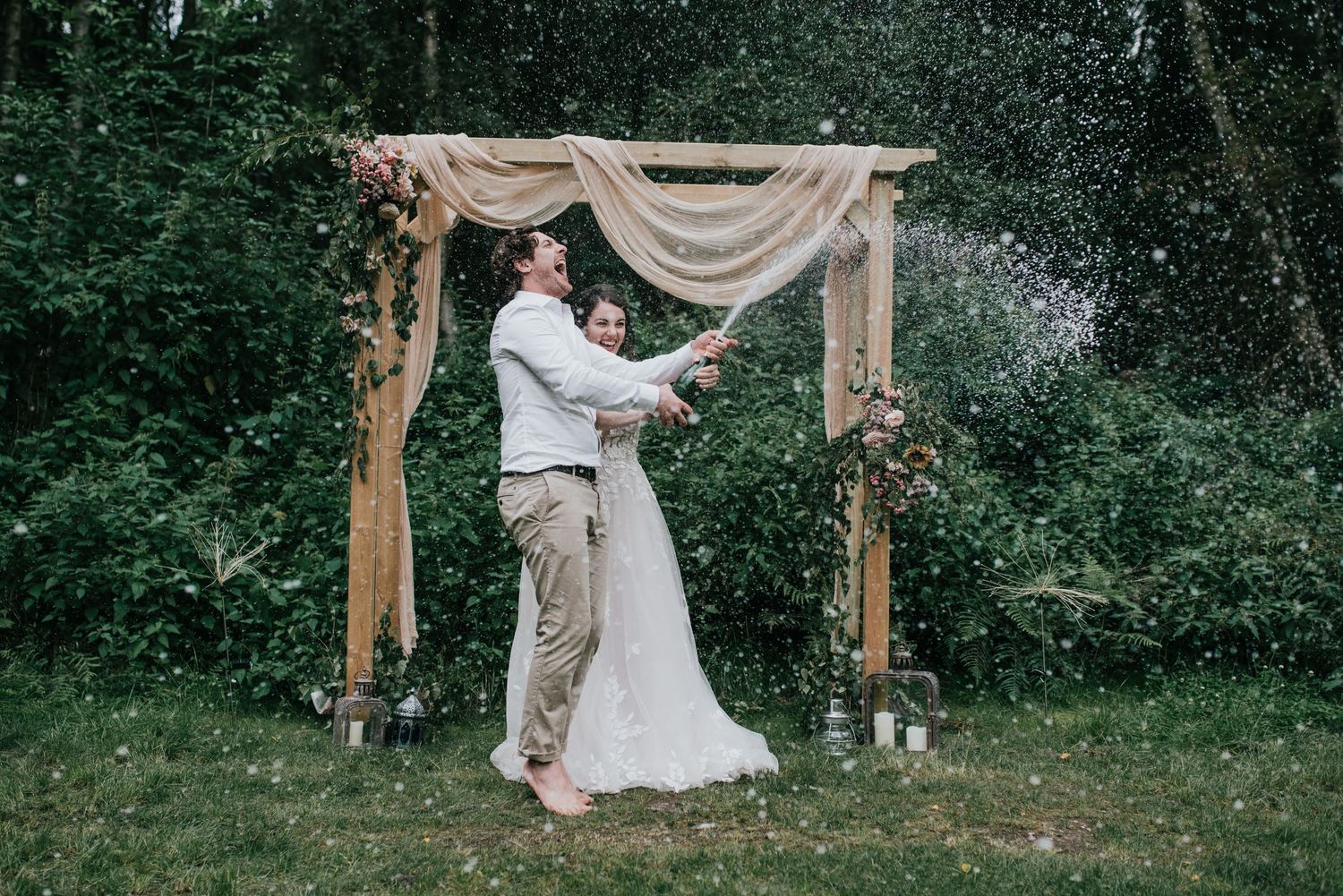 Newlyweds share their first dance under a rustic wooden arch draped with sheer fabric in an outdoor ceremony.