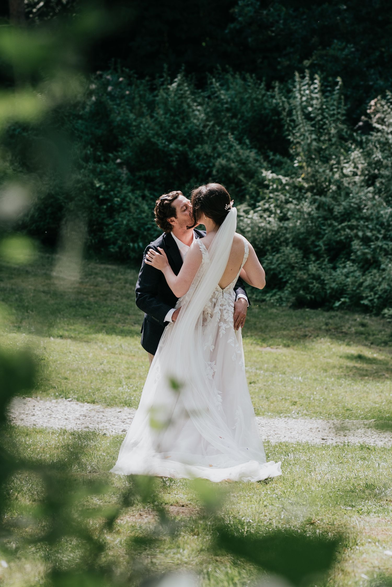 Couple shares romantic moment in sunlit garden setting during wedding celebration.