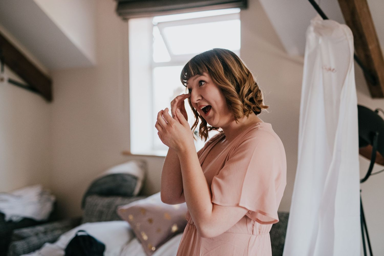 An emotional reaction captured during wedding preparations in a soft pink robe.