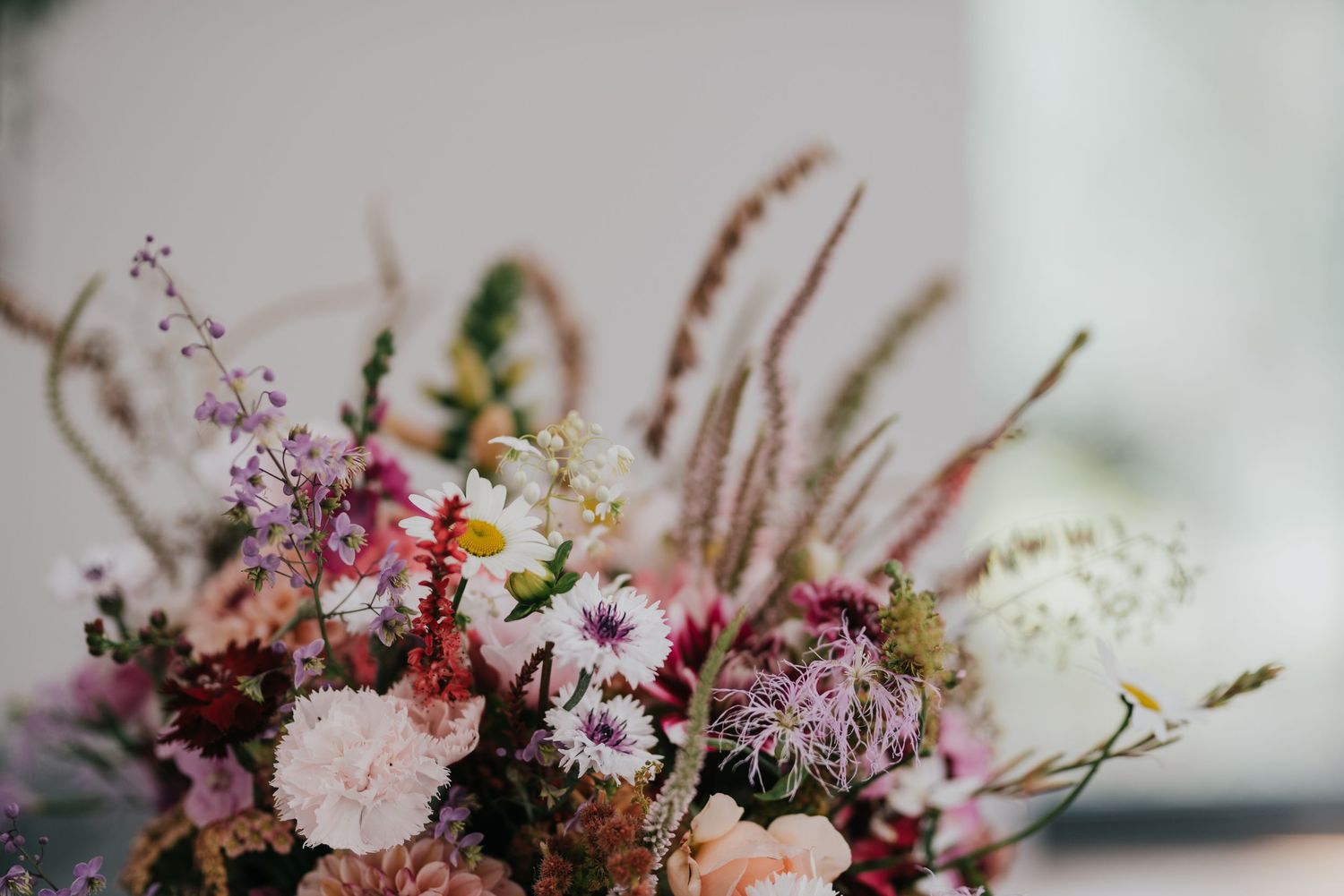 Delicate floral arrangement featuring pink and purple blooms with dried grasses and foliage.