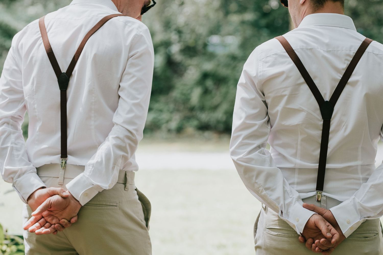 Back view of two people wearing matching white shirts and suspenders standing side by side.