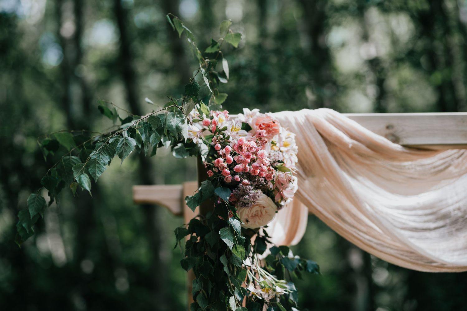 Pink and white flowers with flowing fabric draping on a wedding ceremony arch.