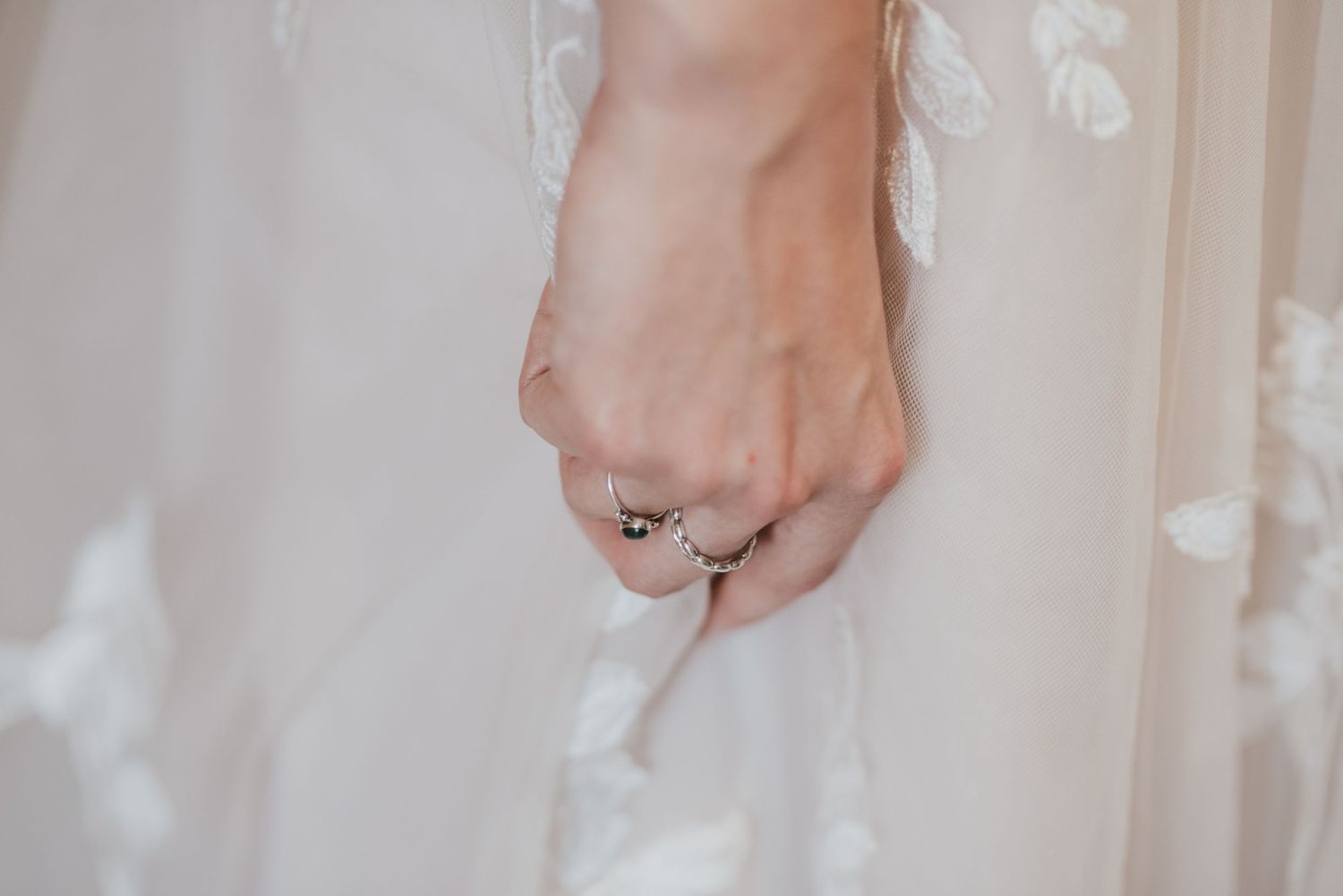 Close-up of a hand wearing an engagement ring against white fabric.