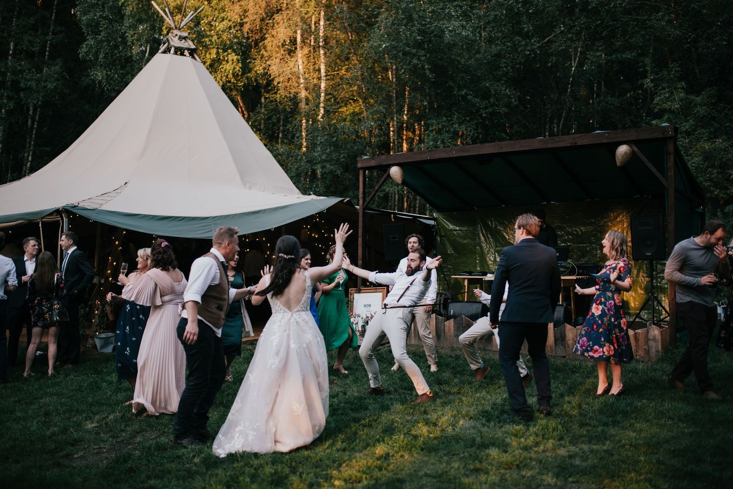 Wedding guests dancing outdoors under a white tent during sunset celebrations.