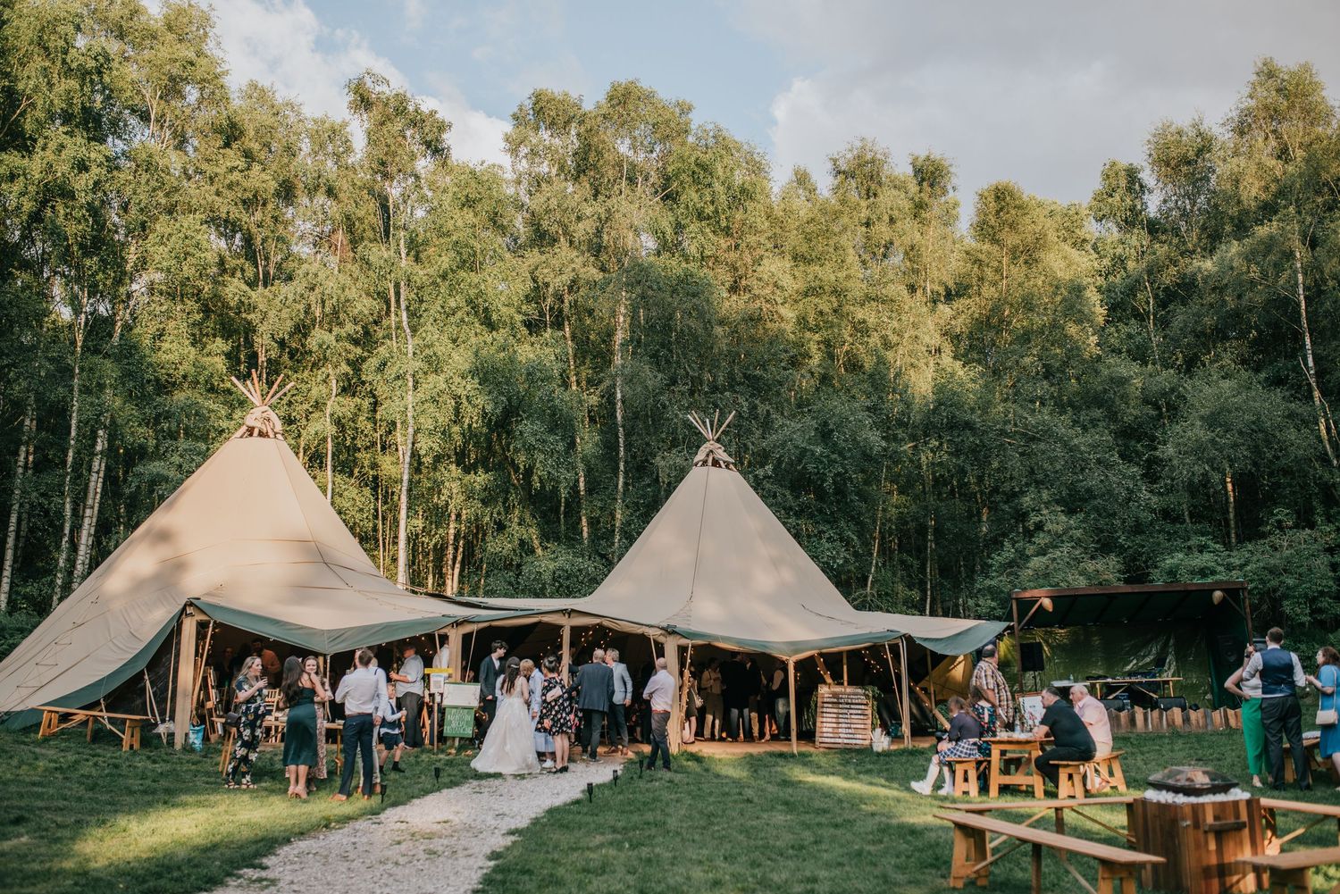 Wedding reception setup with two large teepee-style tents in a scenic forest clearing.