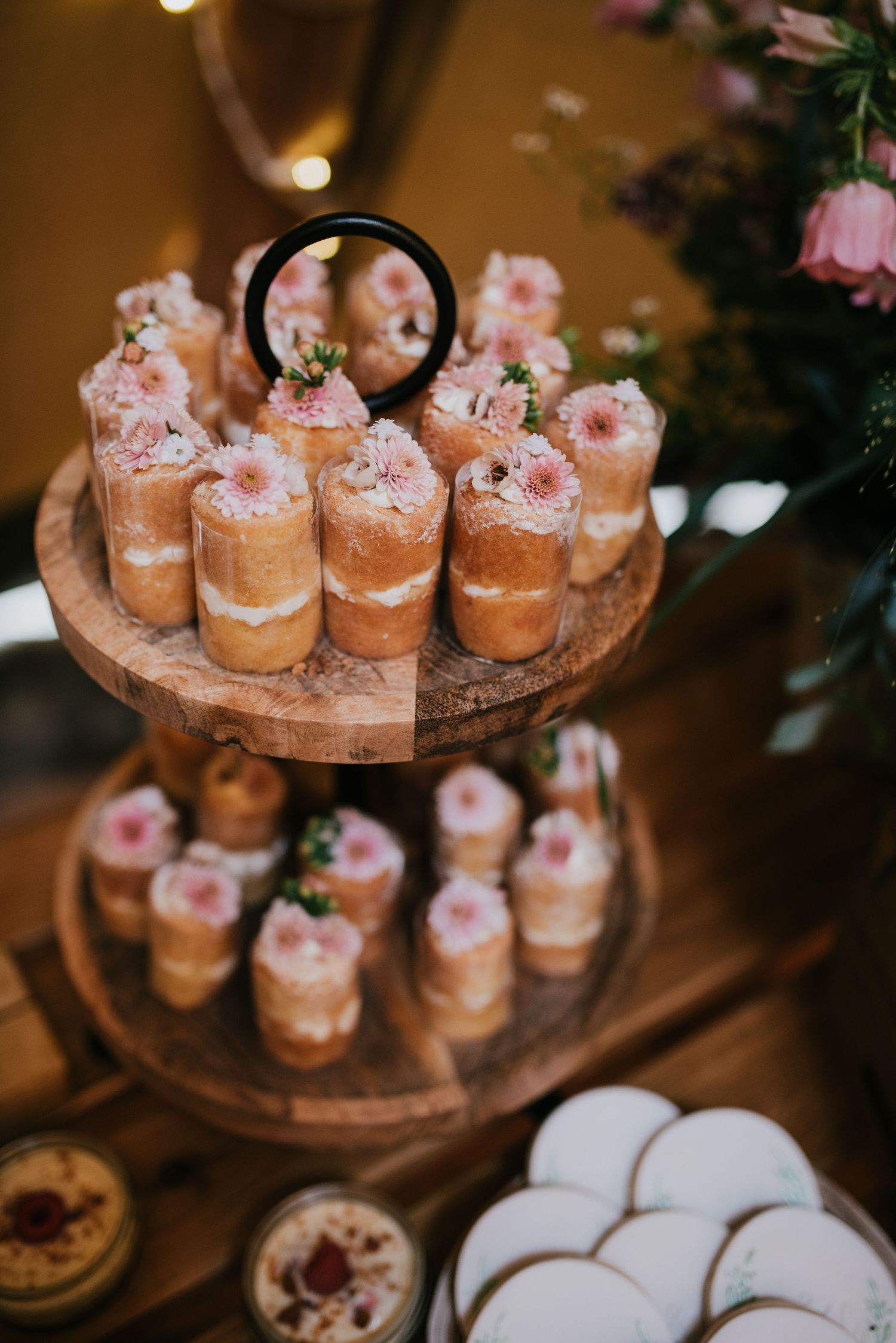 Tiered display of mini desserts garnished with pink flowers on wooden stands.