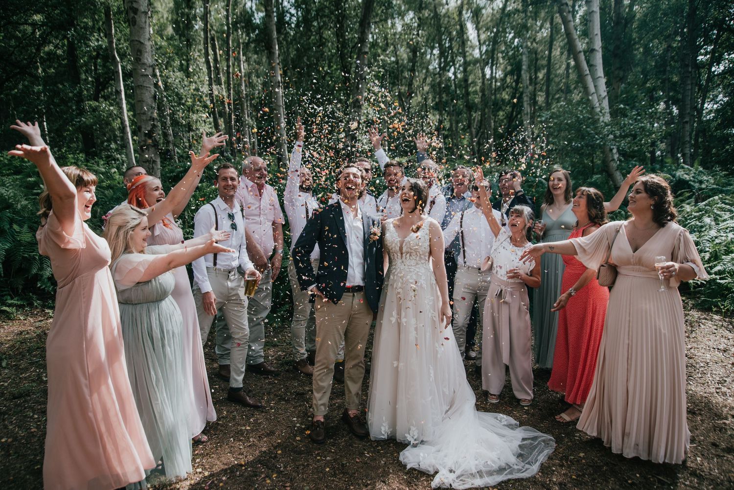 Wedding party celebrating with confetti in a lush forest setting.