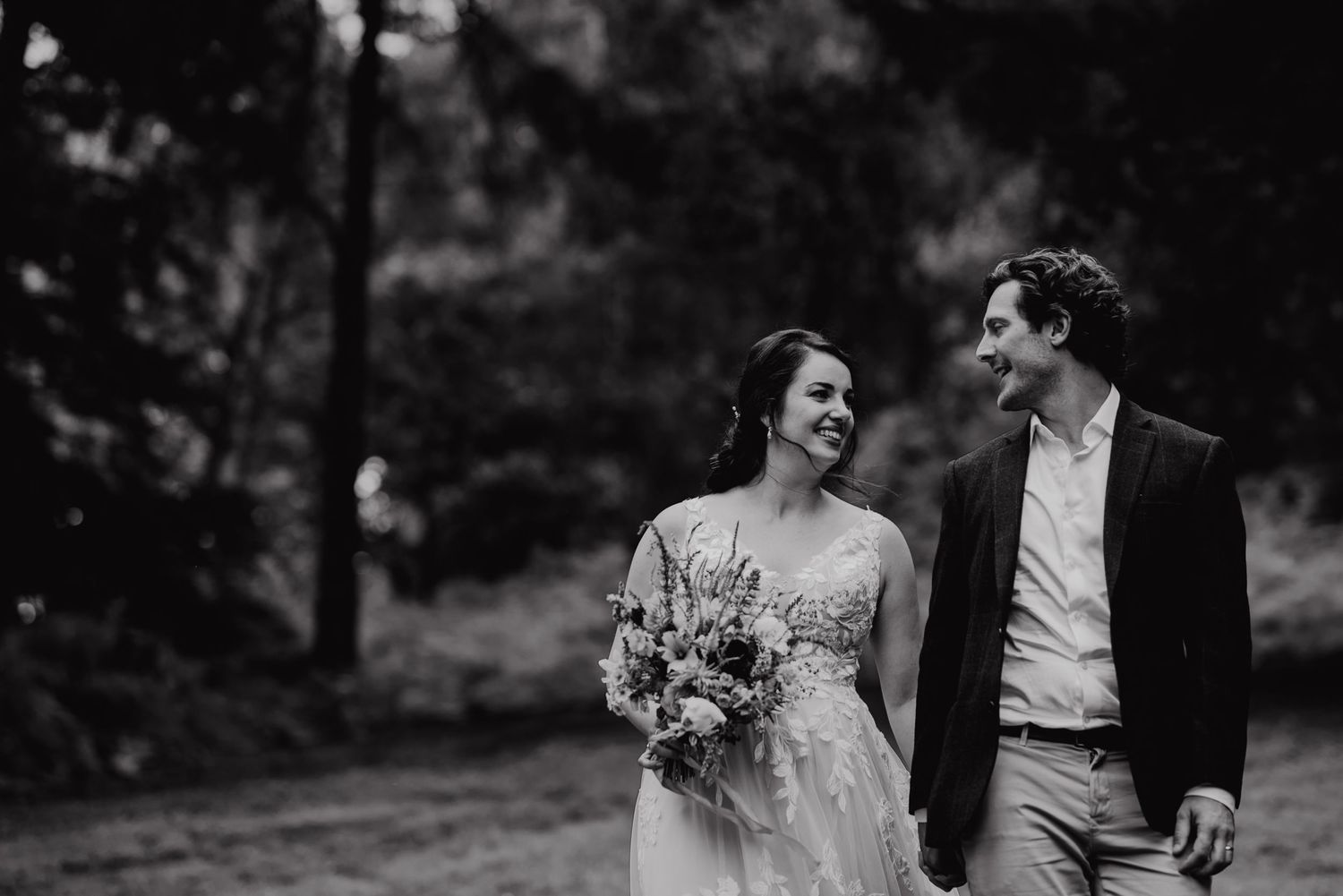 A black and white portrait of a couple sharing laughter while walking together on their wedding day.