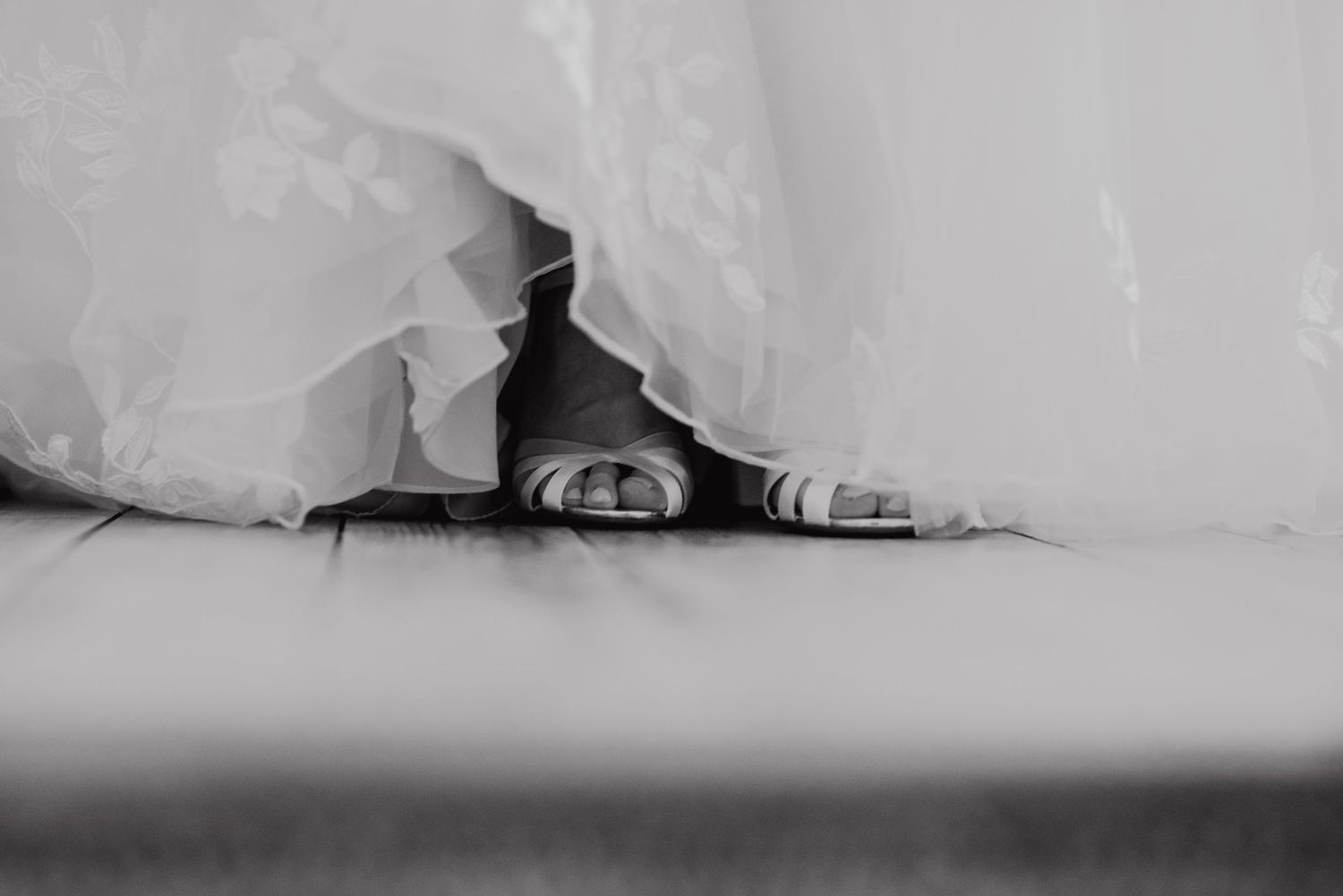 Black and white detail shot of wedding shoes peeking out from under a flowing dress hem.