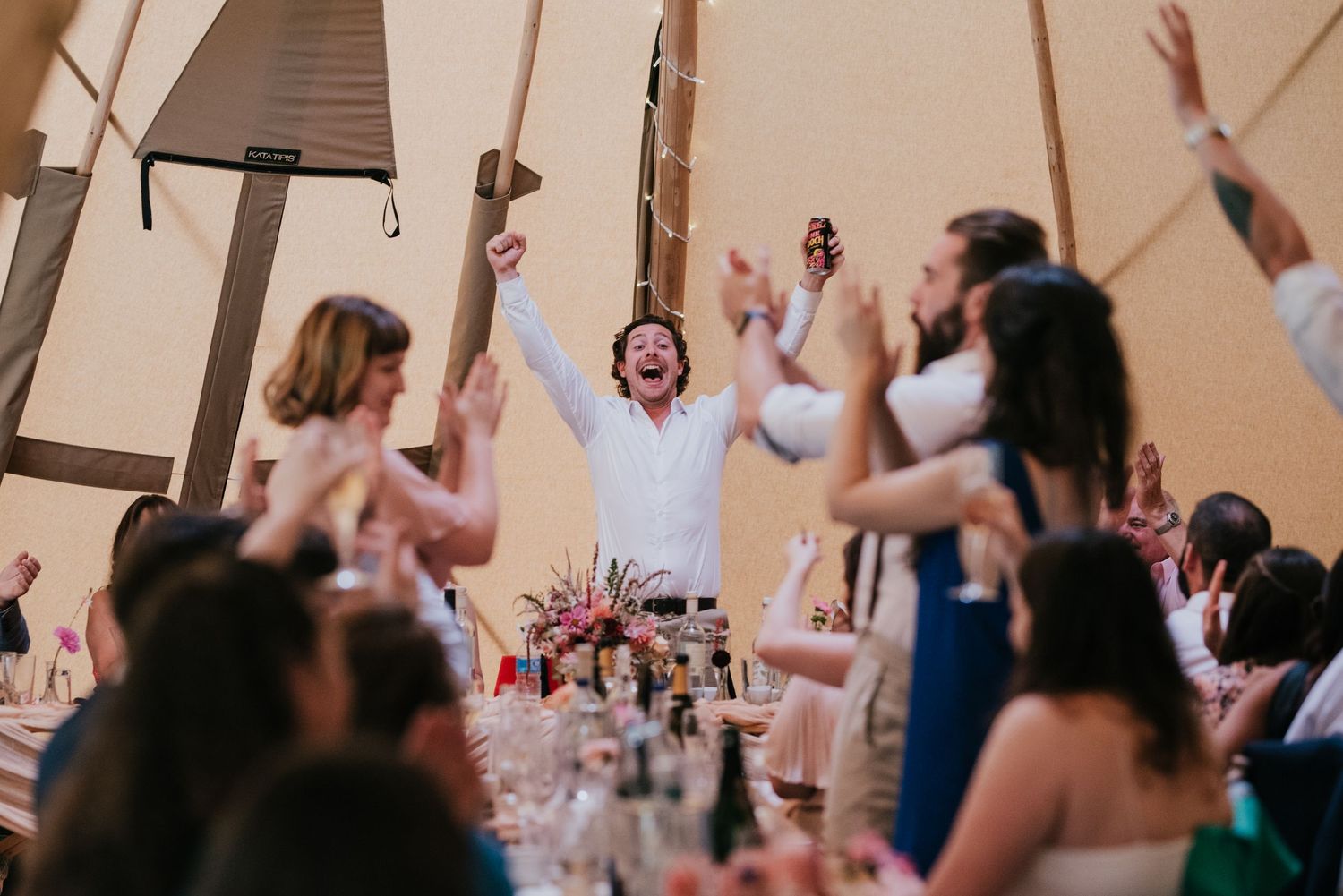 Wedding attendees stand cheering and raising hands during a celebratory moment in the reception tent.