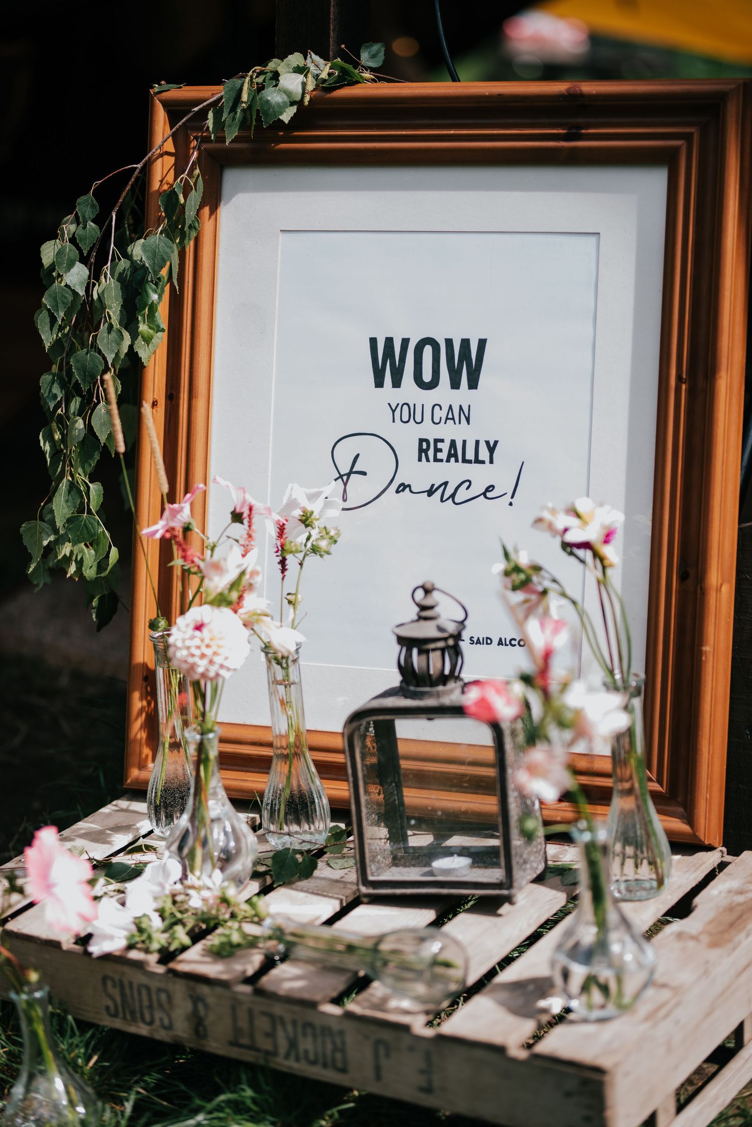 Wedding decor with framed 'WOW you can really Dance!' sign, lantern, and floral arrangements on wooden crate.