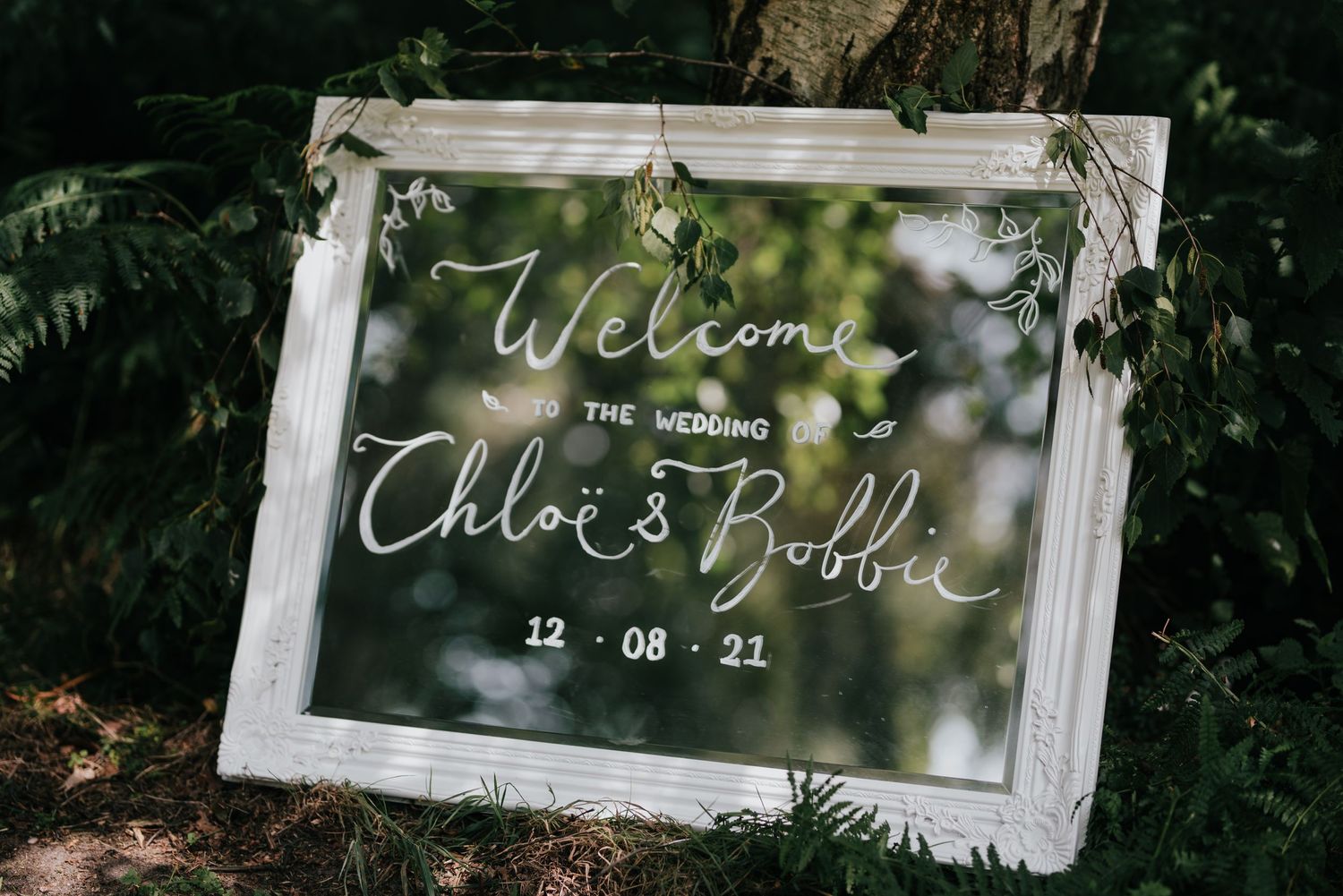 White framed welcome sign with handwritten text for a wedding celebration.