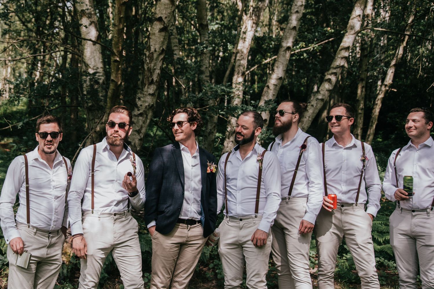 Group of groomsmen in suspenders and casual attire posing against a forest backdrop.