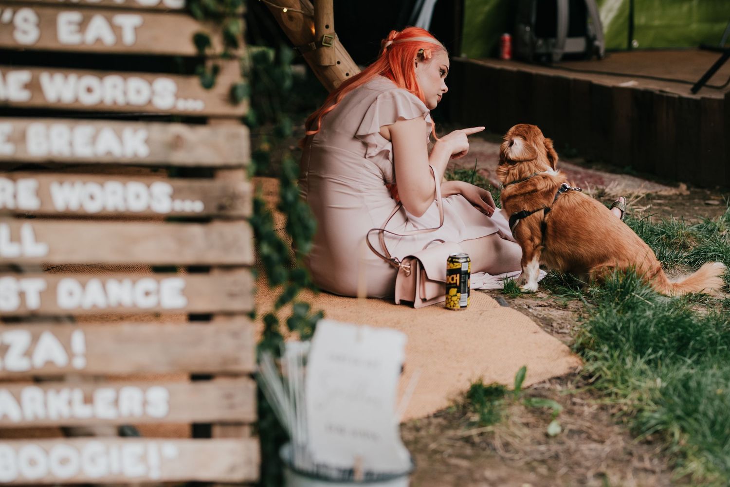Person in pink sits with their golden retriever next to wooden signage outdoors.