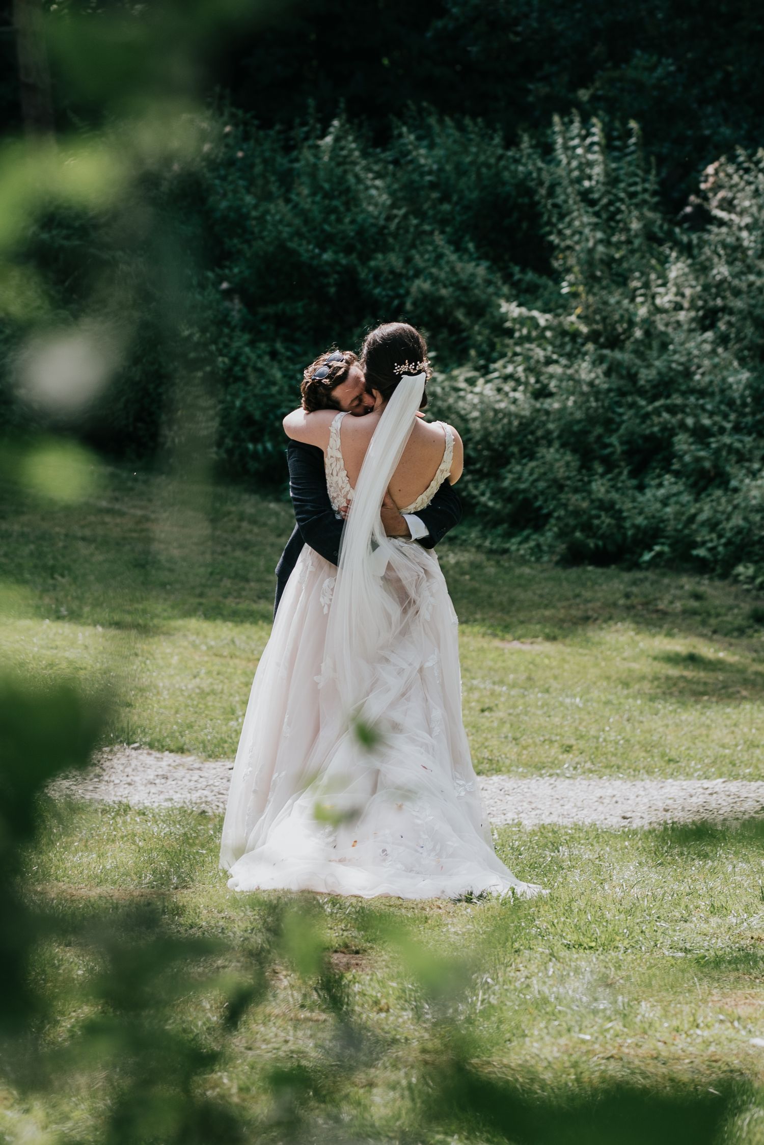 Couple embraces on garden path with flowing white wedding dress and veil.