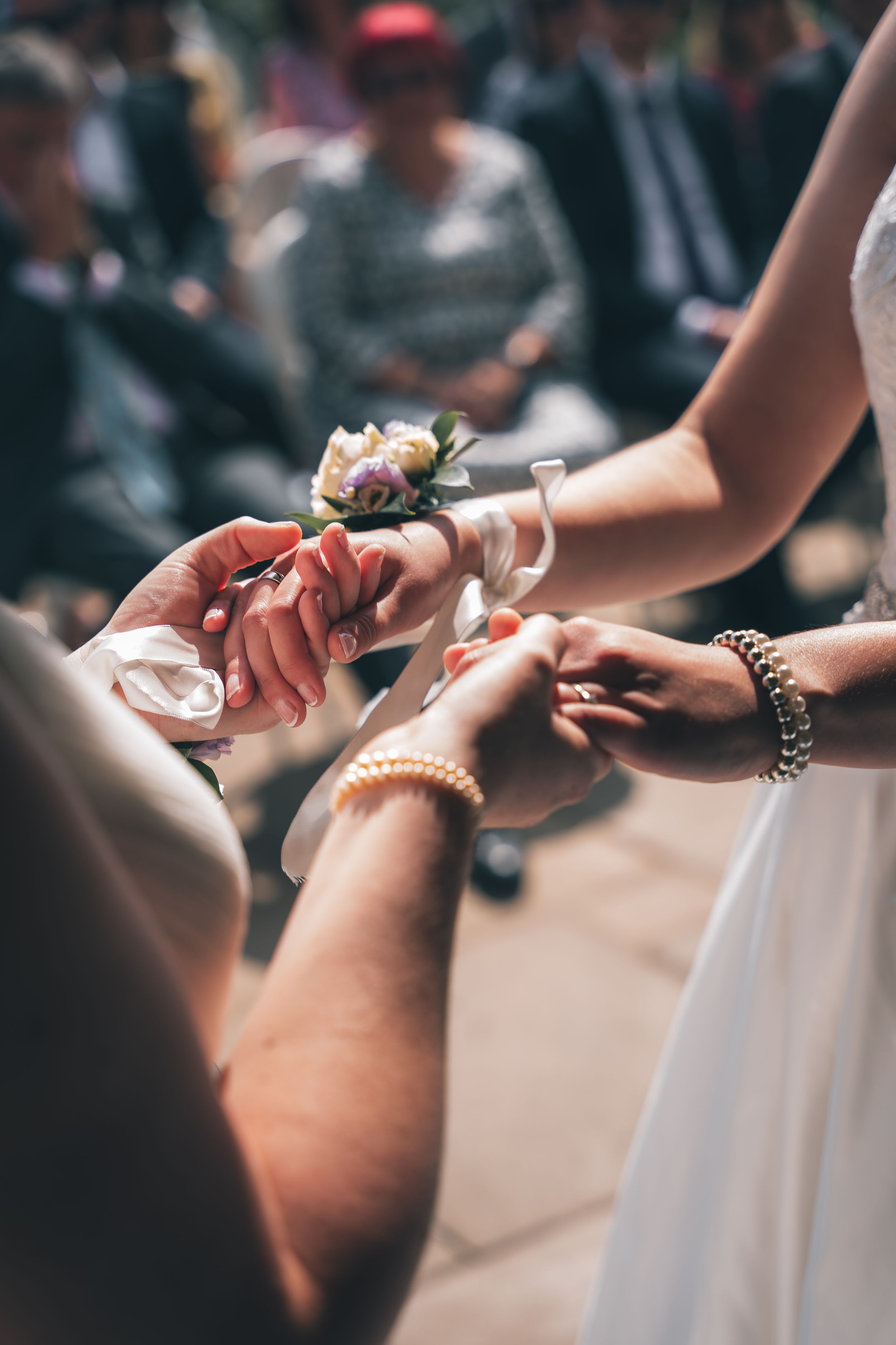 Wedding ceremony detail showing hands exchanging rings with pearl bracelets.