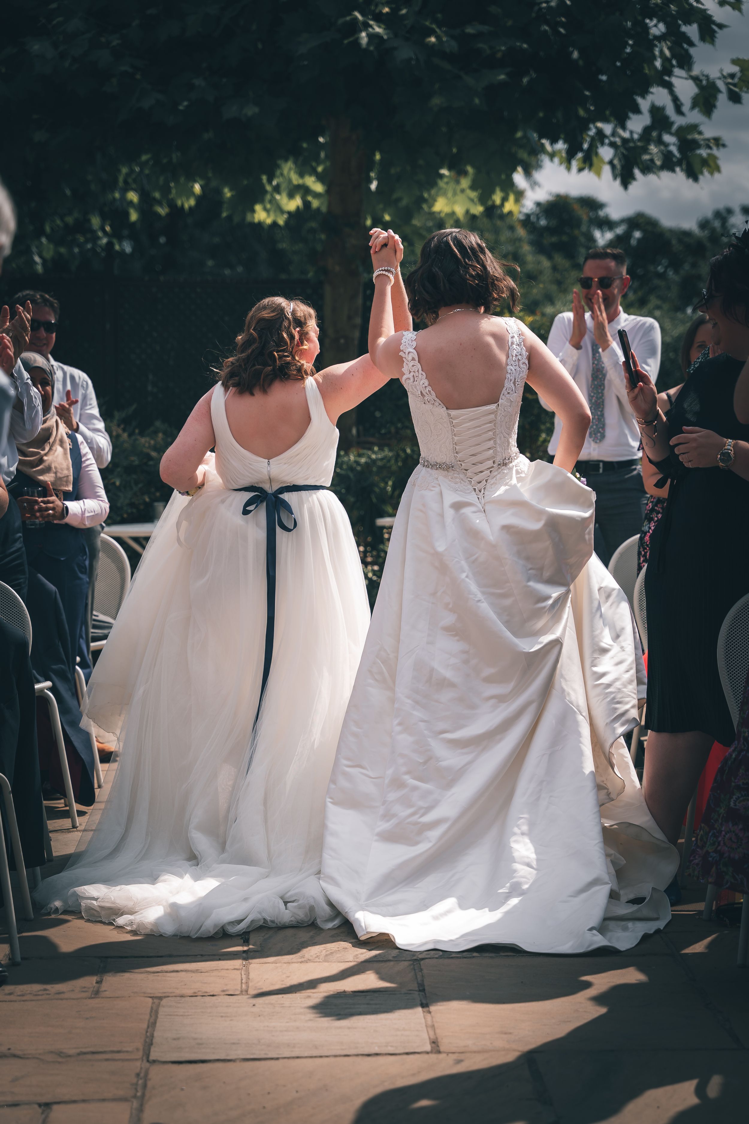 Row of brides in white dresses lined up outdoors during a group wedding event.