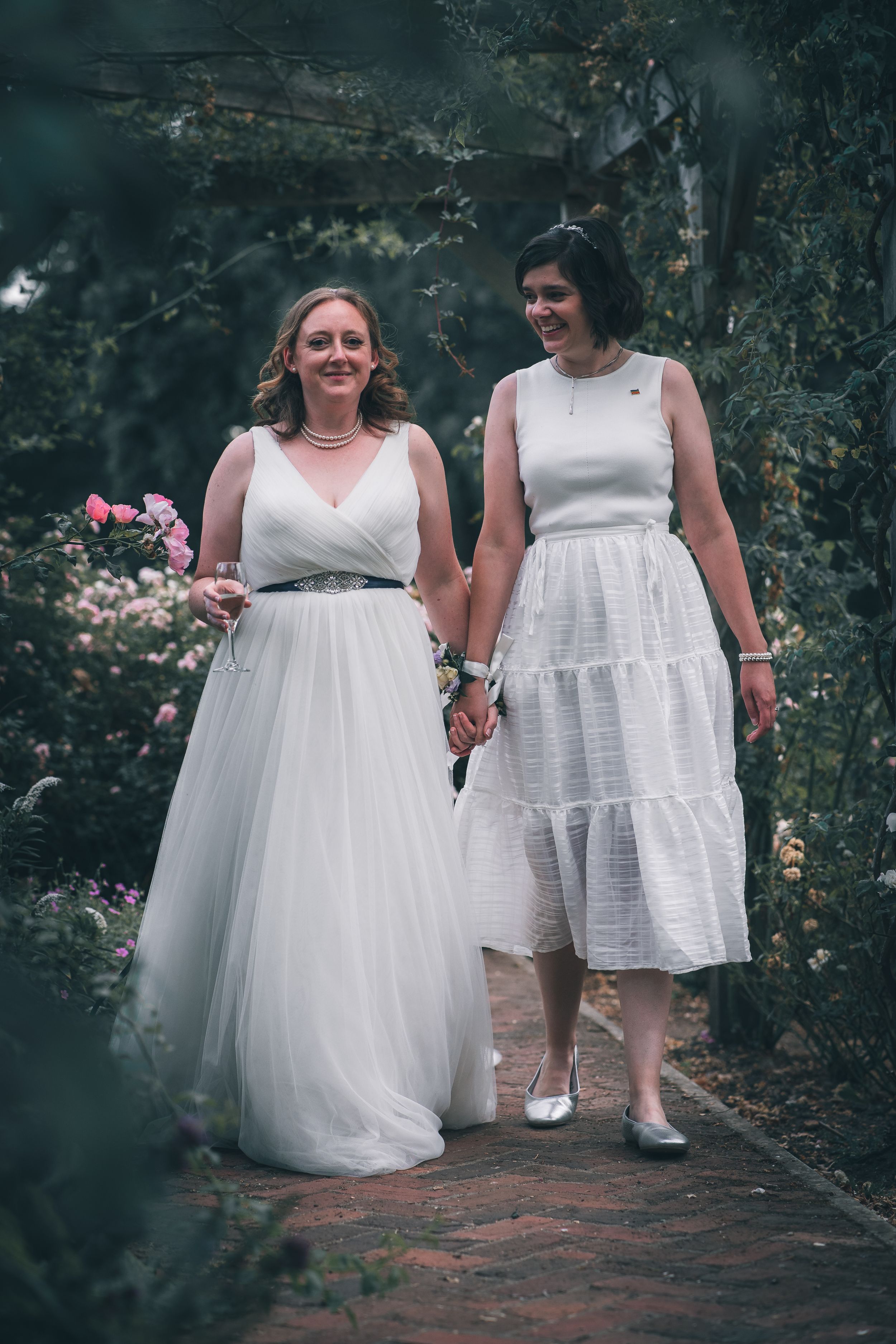 Two people in white dresses walk together along a garden path.