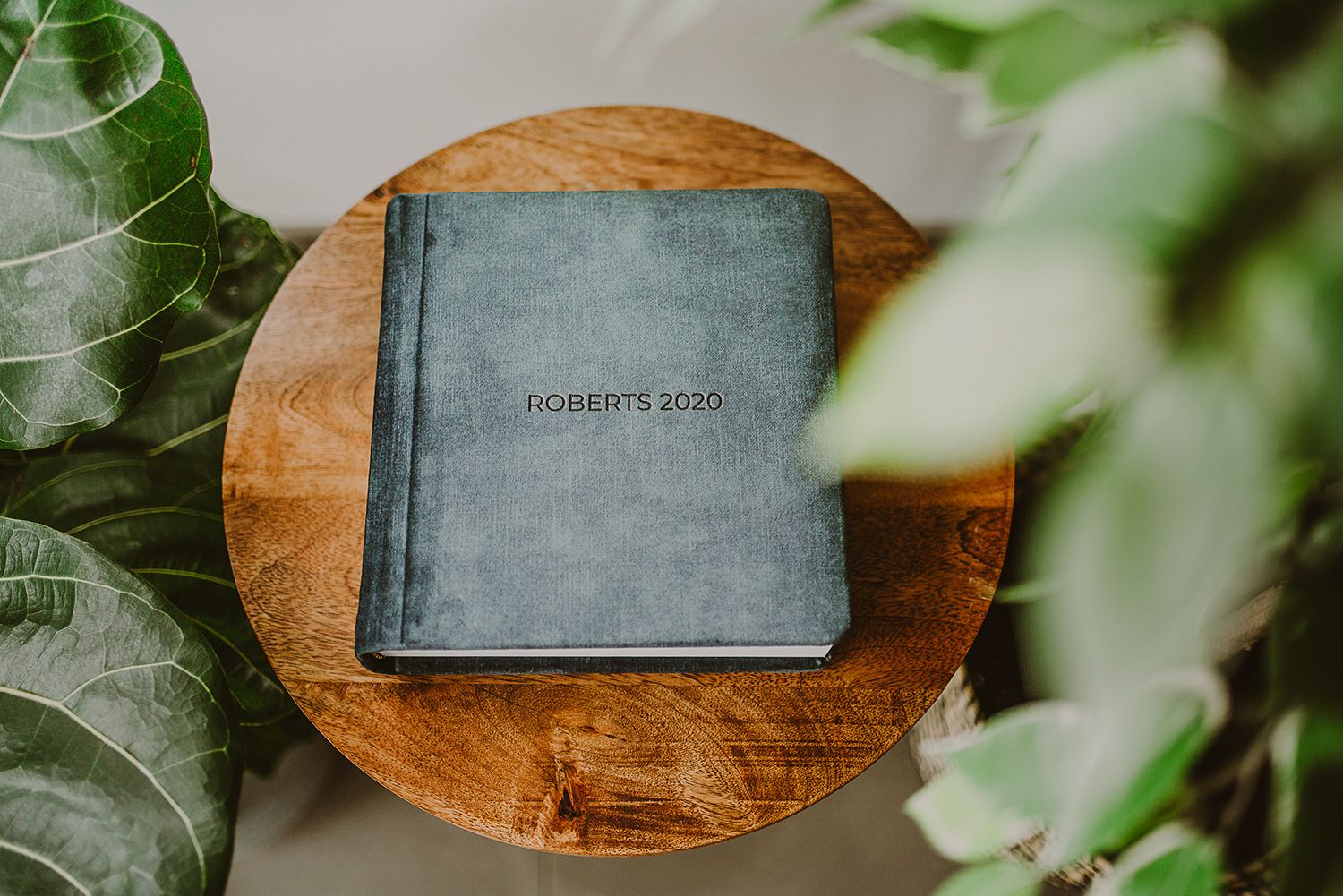 Dark grey moments book placed on wooden surface with green plant leaves in background.