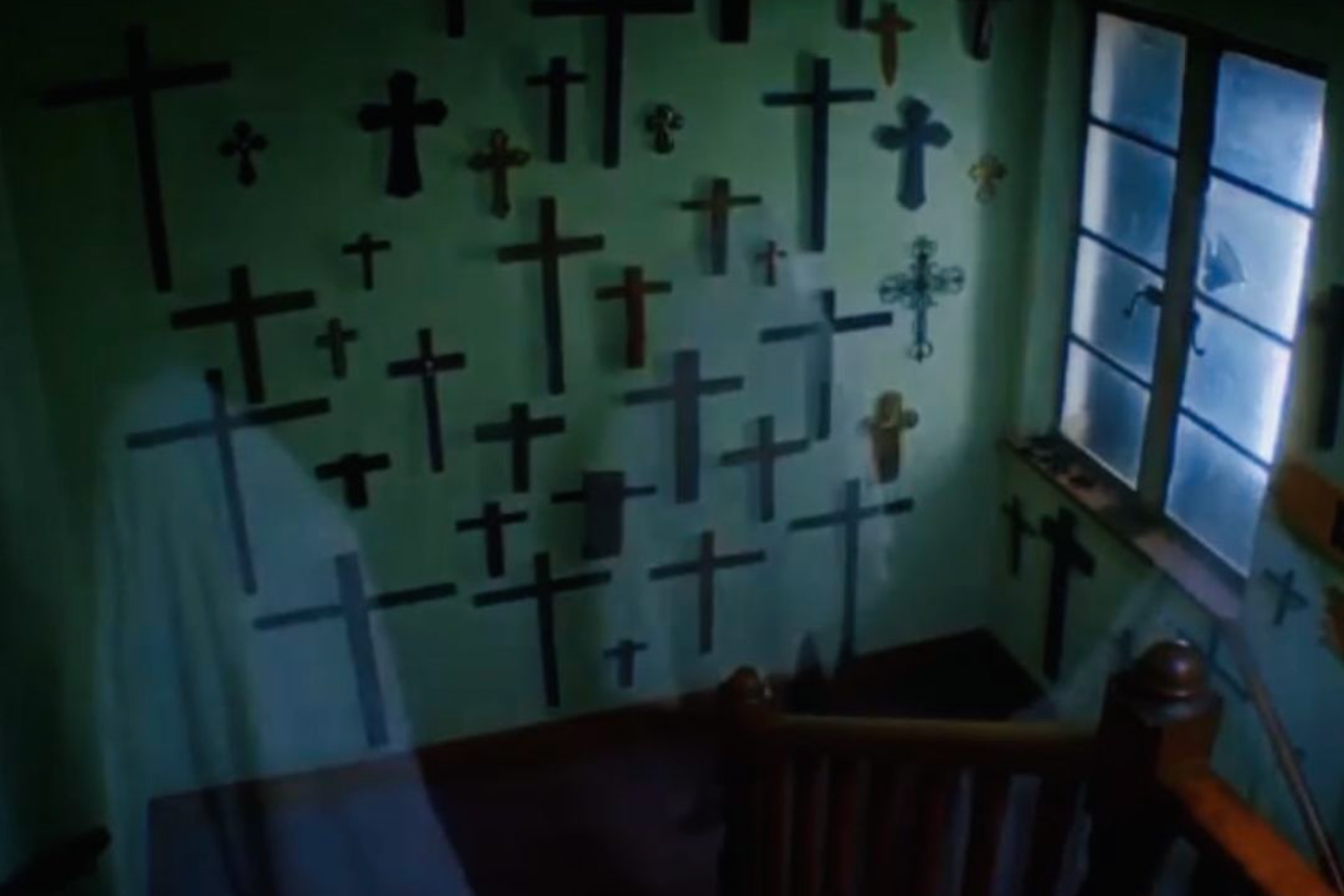 Dark room with multiple crosses mounted on wall creating an eerie religious atmosphere.