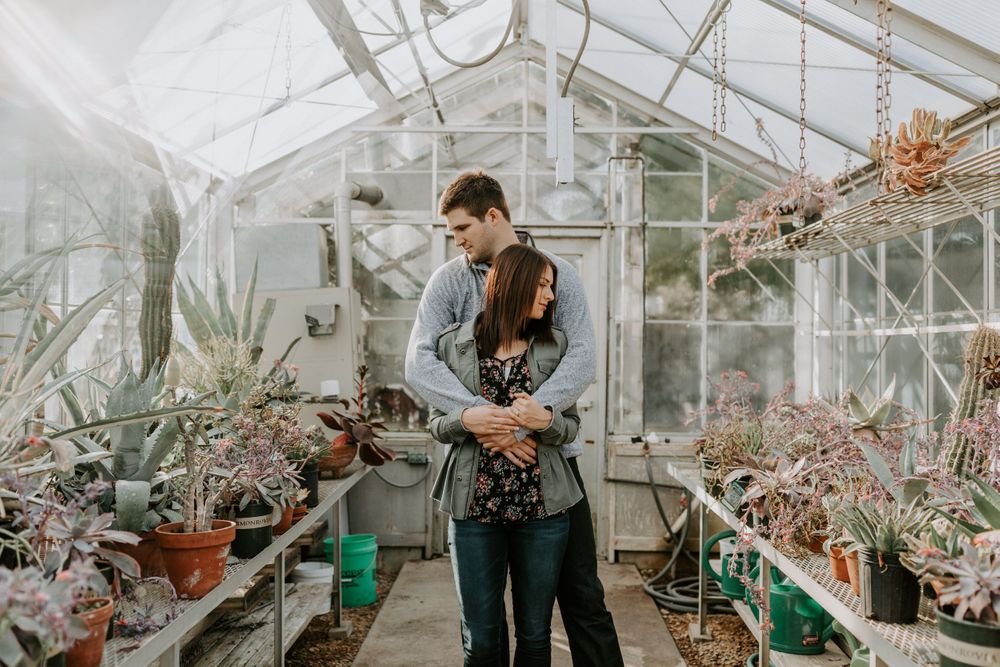 A romantic moment shared in a greenhouse filled with various plants and flowers.