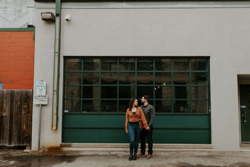 Couple poses together in front of industrial building with green garage door.