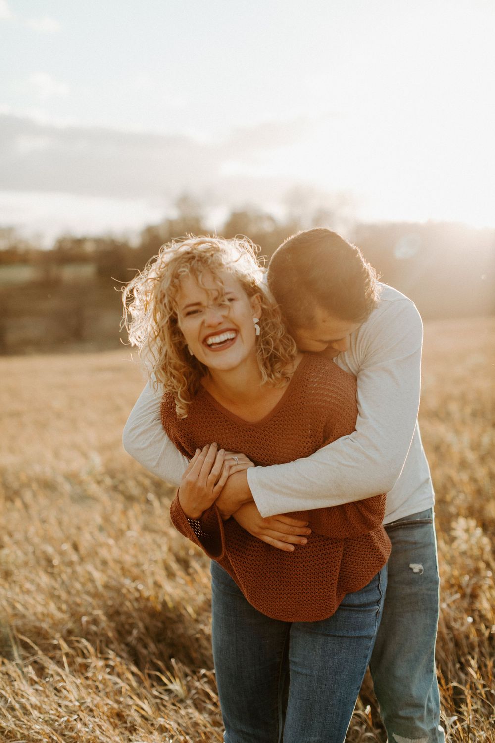 Candid moment of laughter and embrace in golden field at sunset.