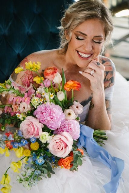 Bride laughing while holding a very colorful boutique and siting on a velvet chair