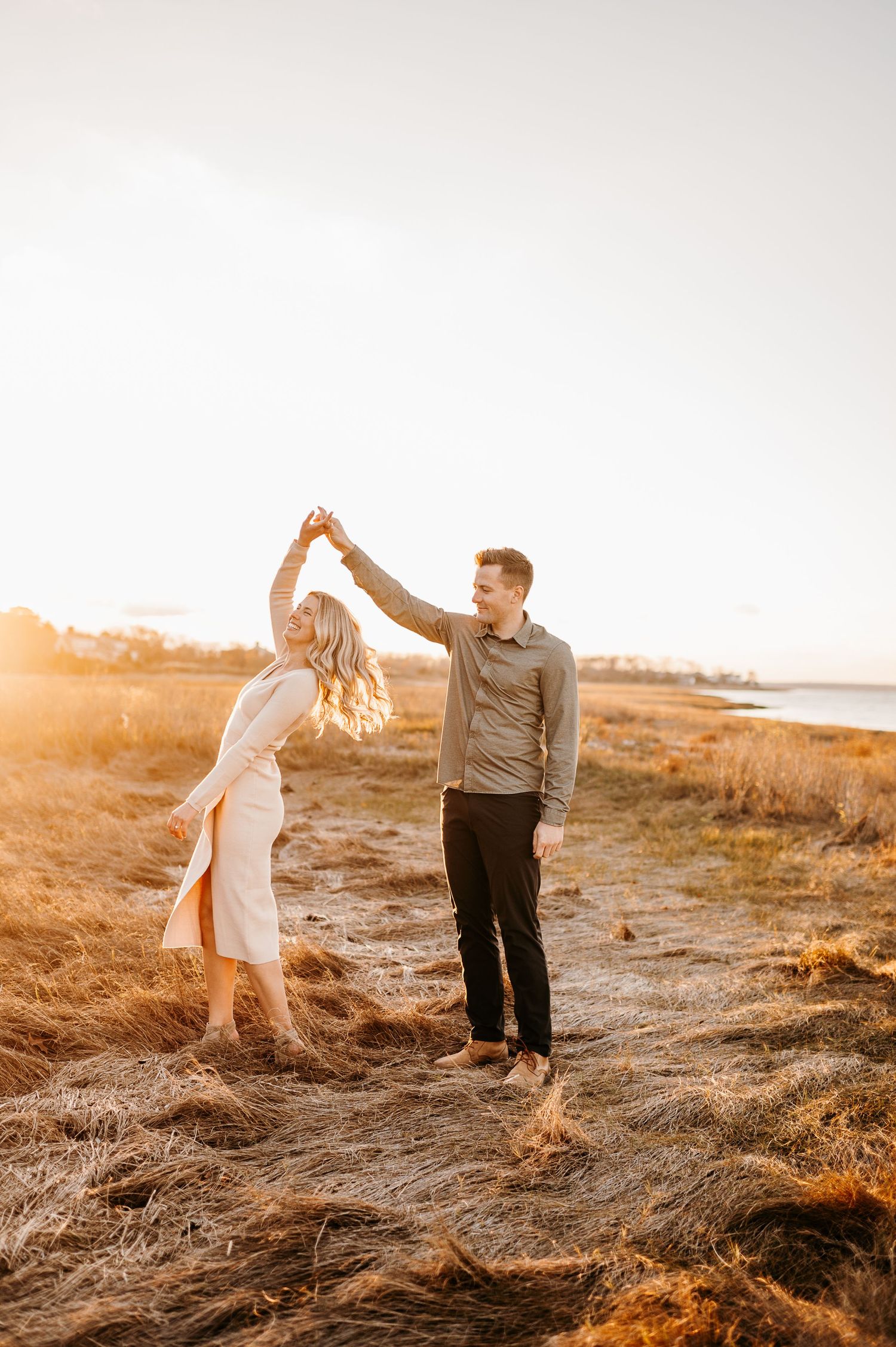 A couple dances playfully in a field during sunset, creating joyful silhouettes.