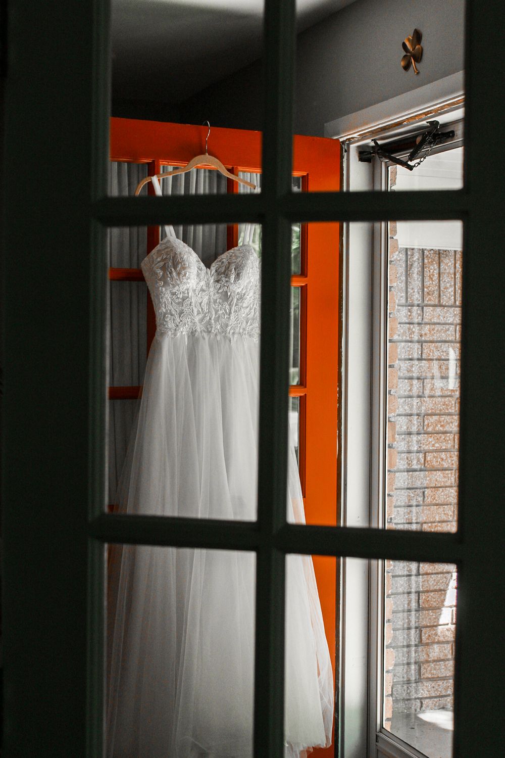 A white wedding gown displayed against an orange wall near windows.