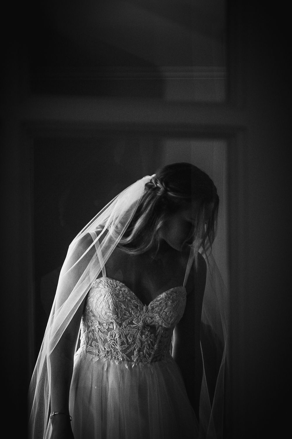 Close-up of a lace wedding dress bodice with veil in dramatic black and white lighting.