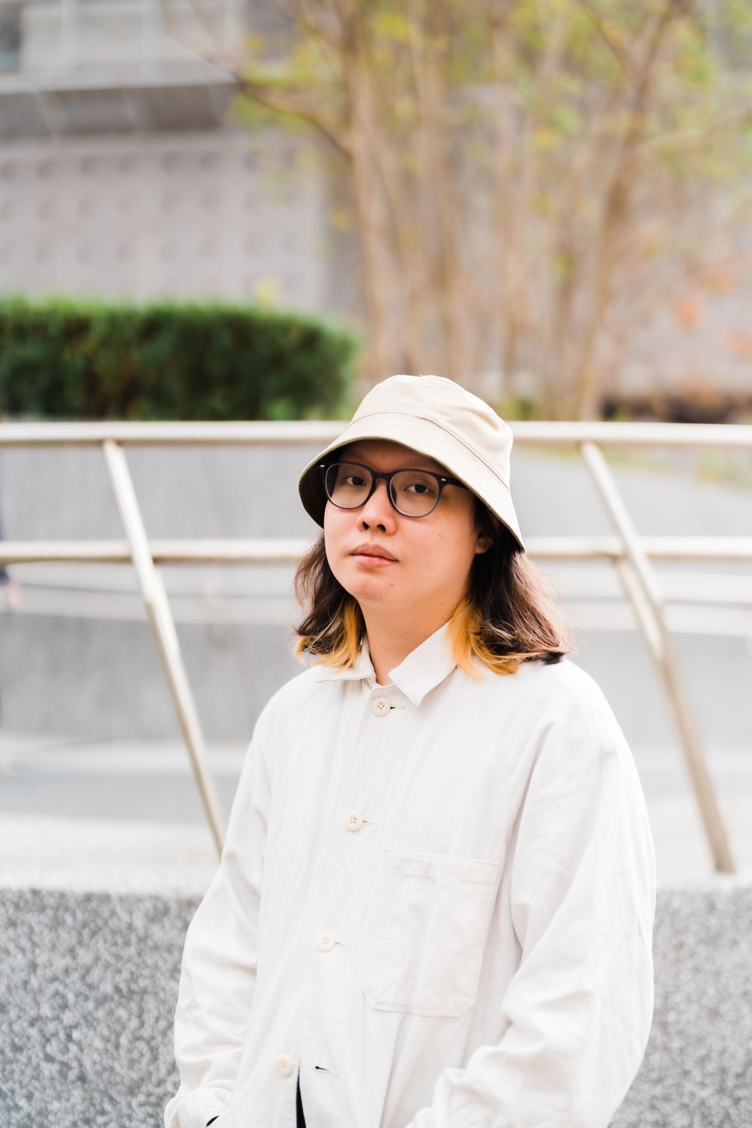 Person wearing bucket hat and white coat standing in urban setting.