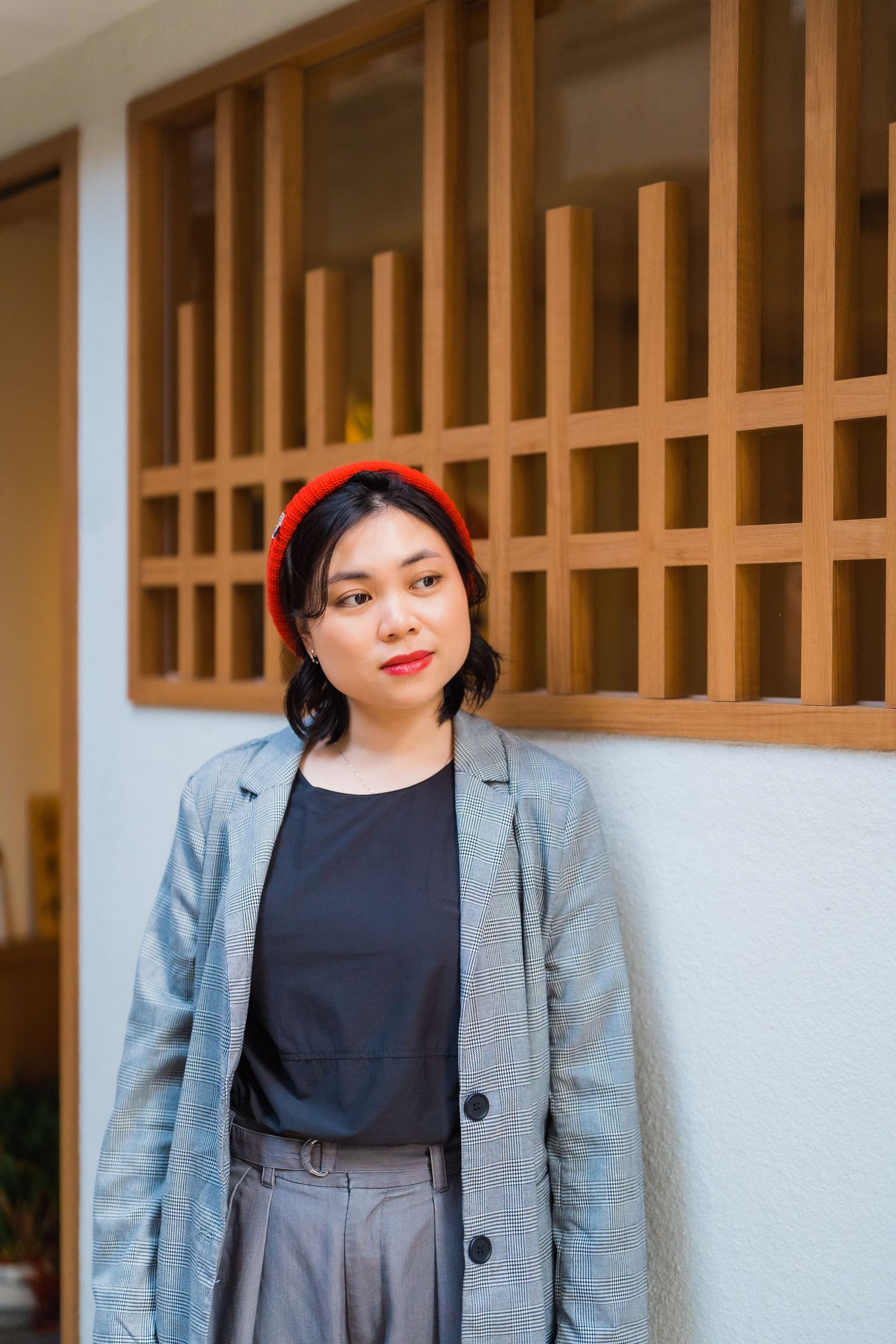 Fashion portrait with red beret and gray blazer against wooden lattice wall.