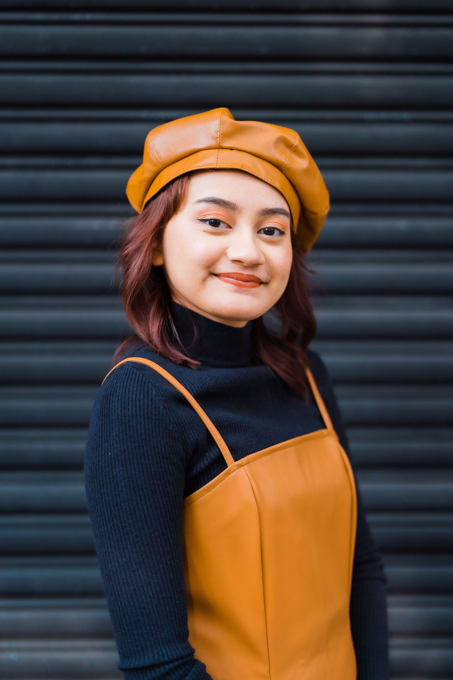 Portrait against black shutters wearing orange beret and navy turtleneck.