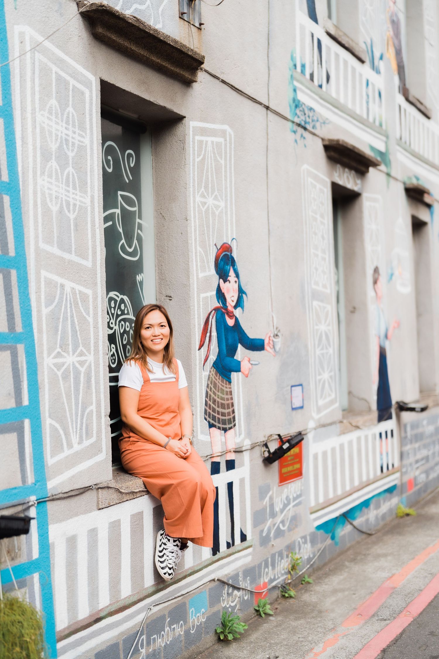 Person in orange overalls sitting on ledge beside street art mural.