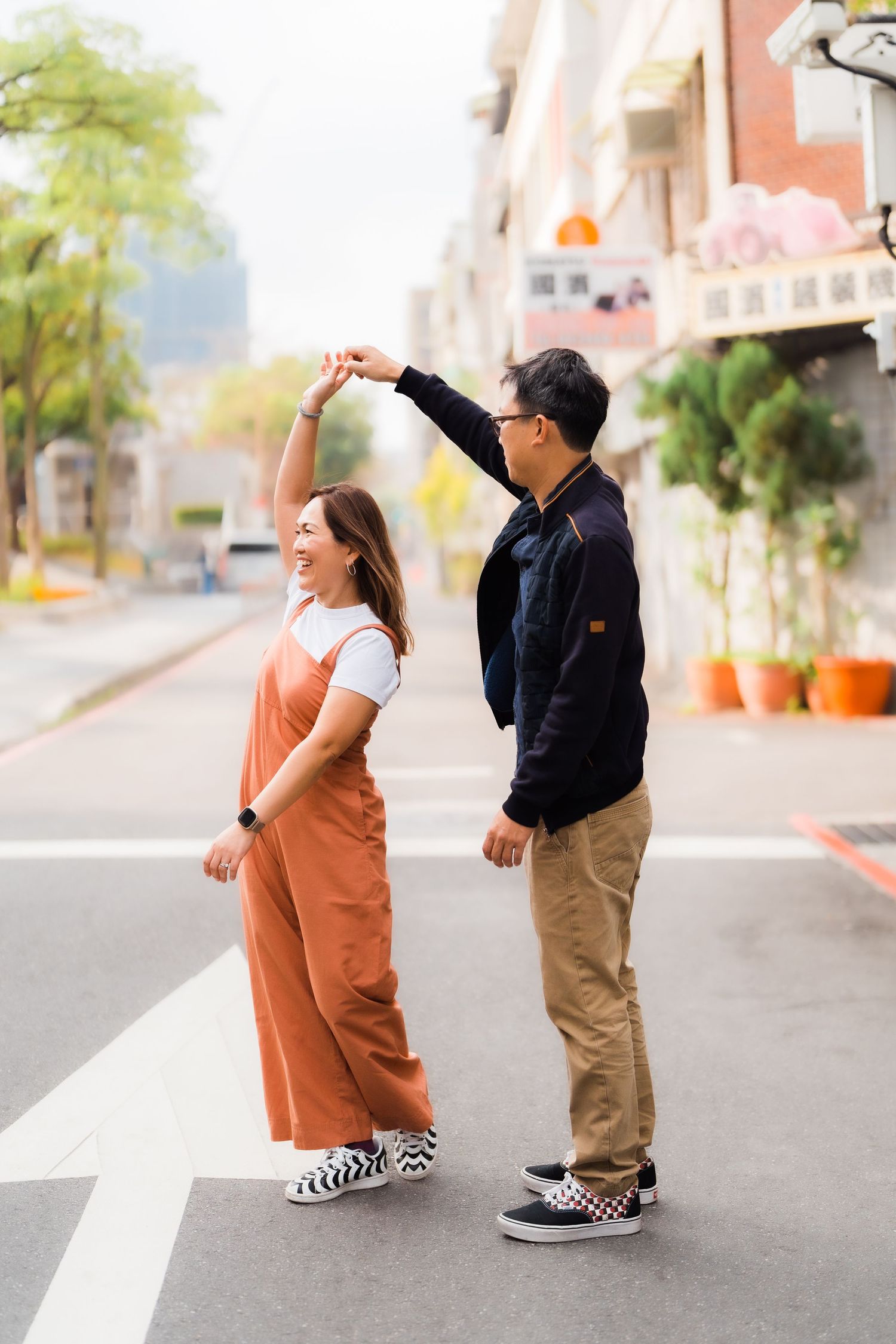 Couple dancing playfully on city street wearing casual outfits.