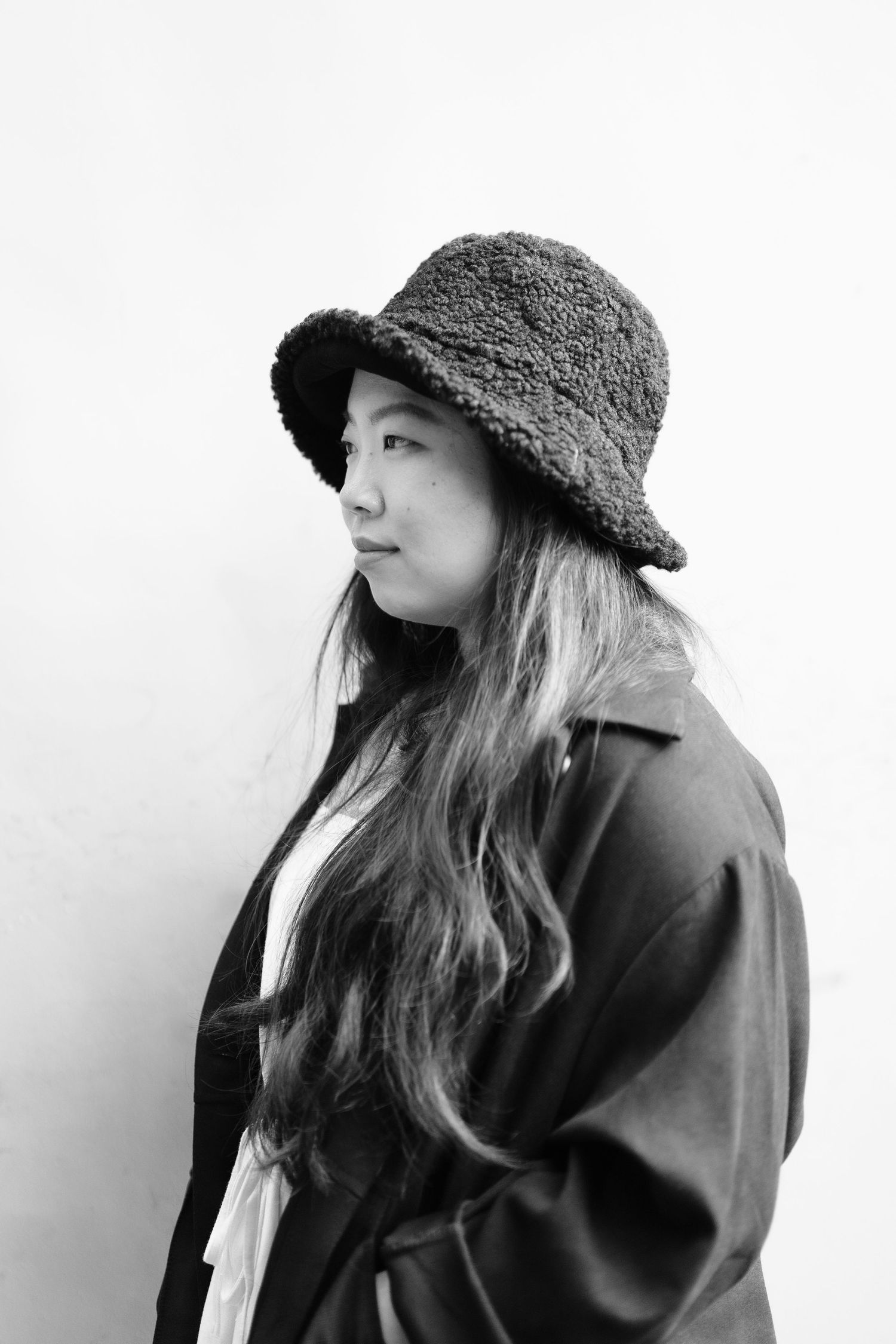 Stylish portrait of person in black coat and bucket hat against white background.