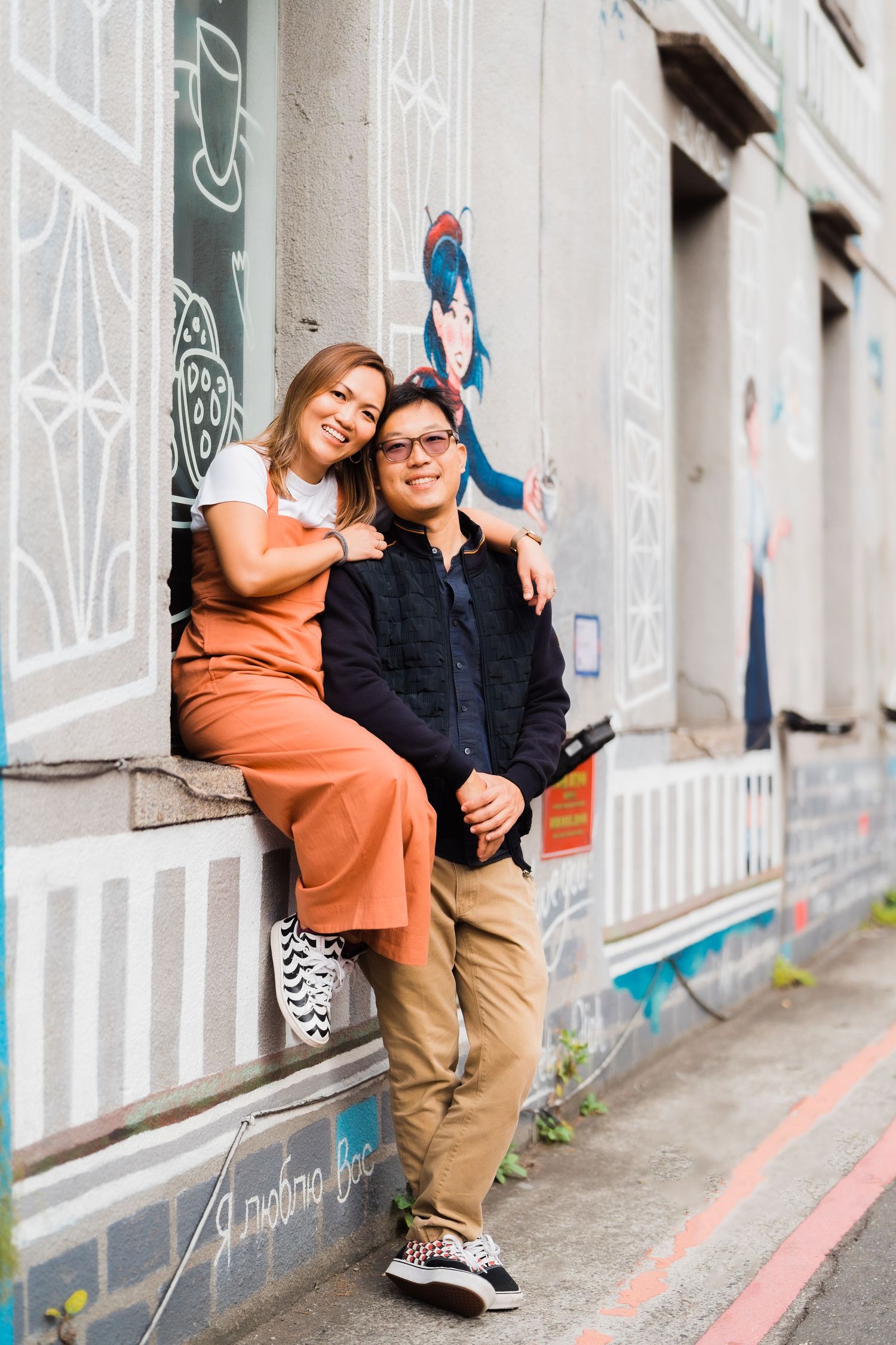 A couple sits casually against a graffiti wall in an urban setting.