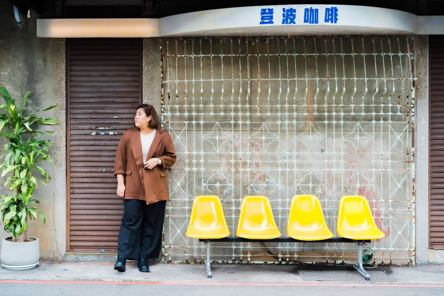 Person in brown coat standing by yellow seats at a storefront in Asia.