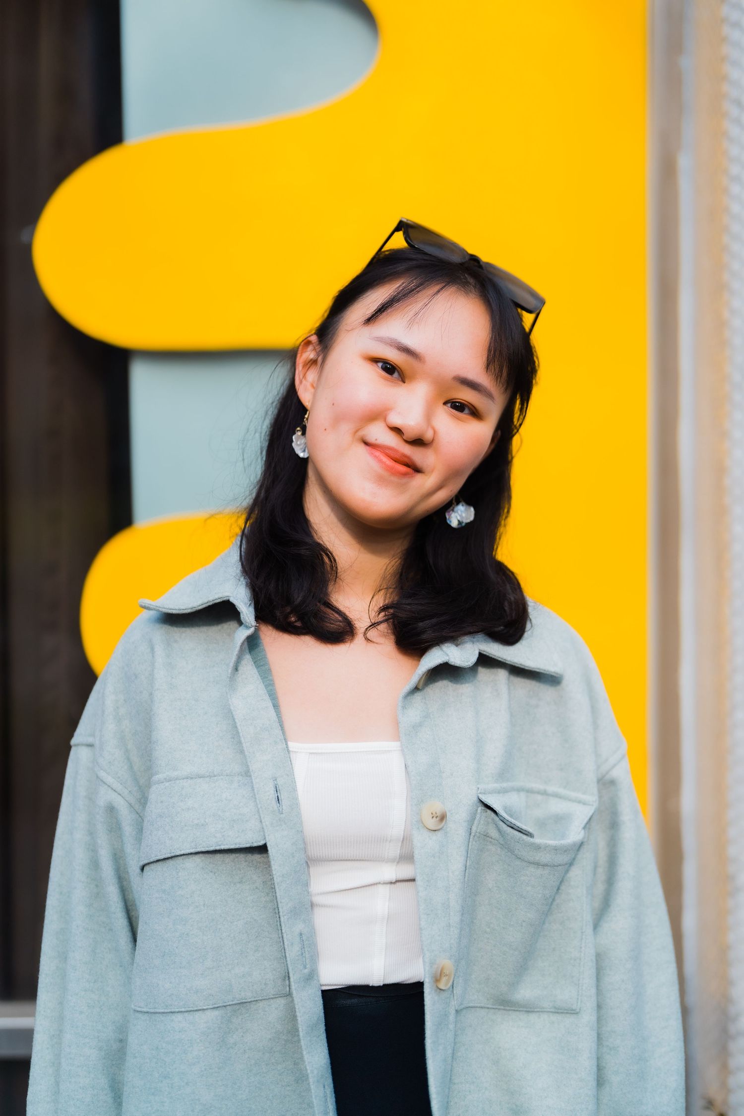 Casual portrait with light denim jacket and white top against vibrant yellow background.