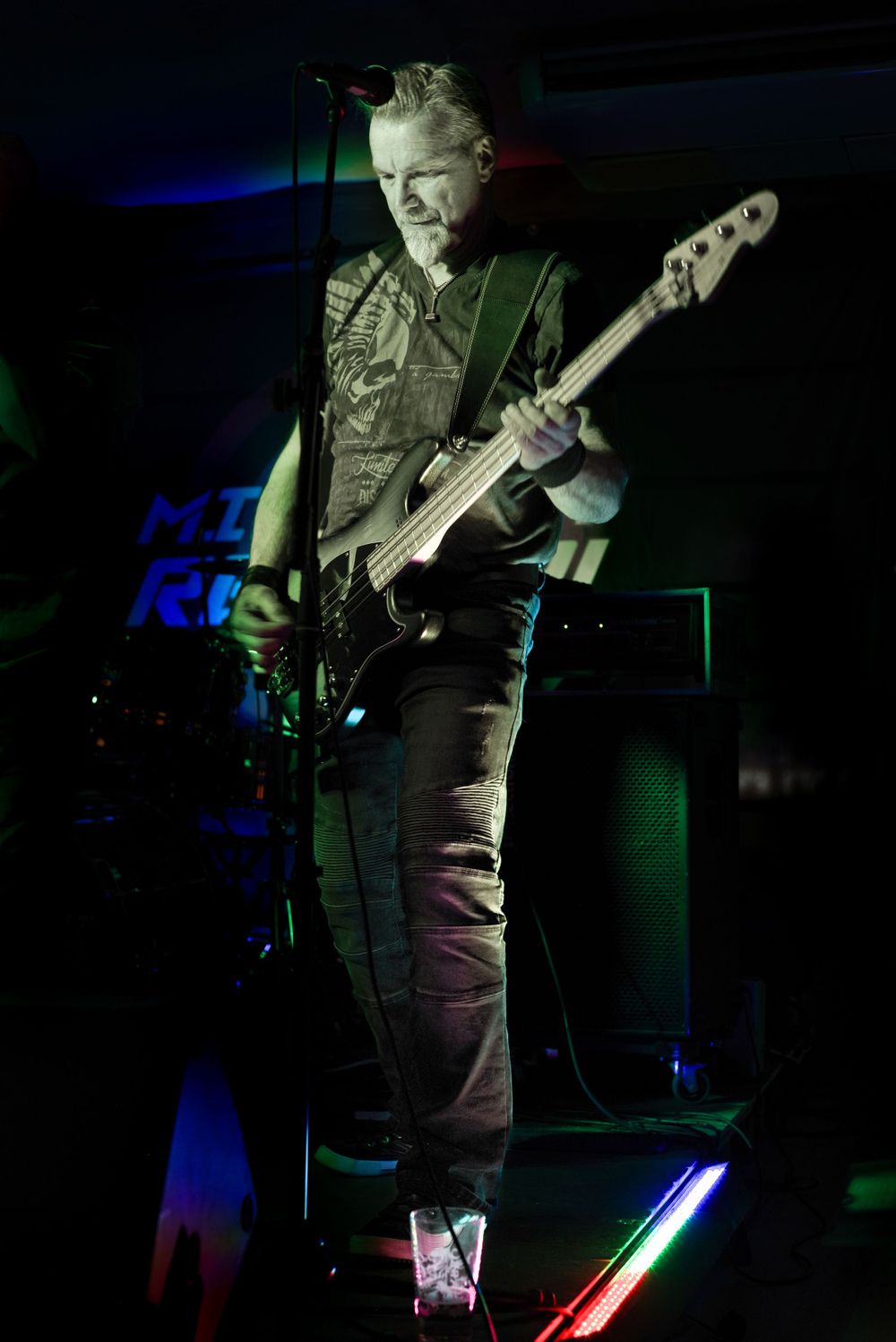 Bass player performs on stage with colorful blue and green lighting effects.
