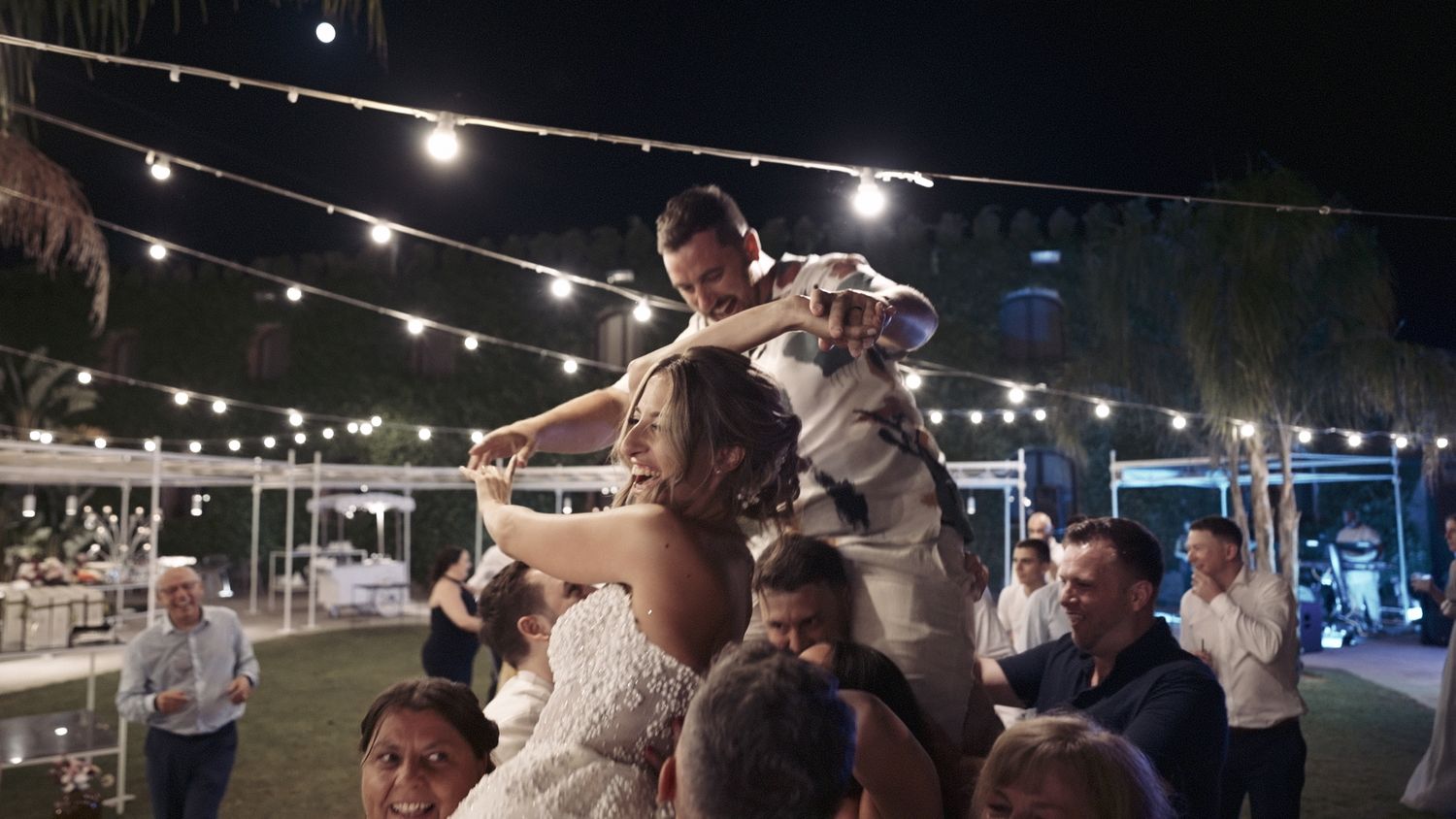 Wedding celebration with dancing and string lights creating a festive outdoor atmosphere.