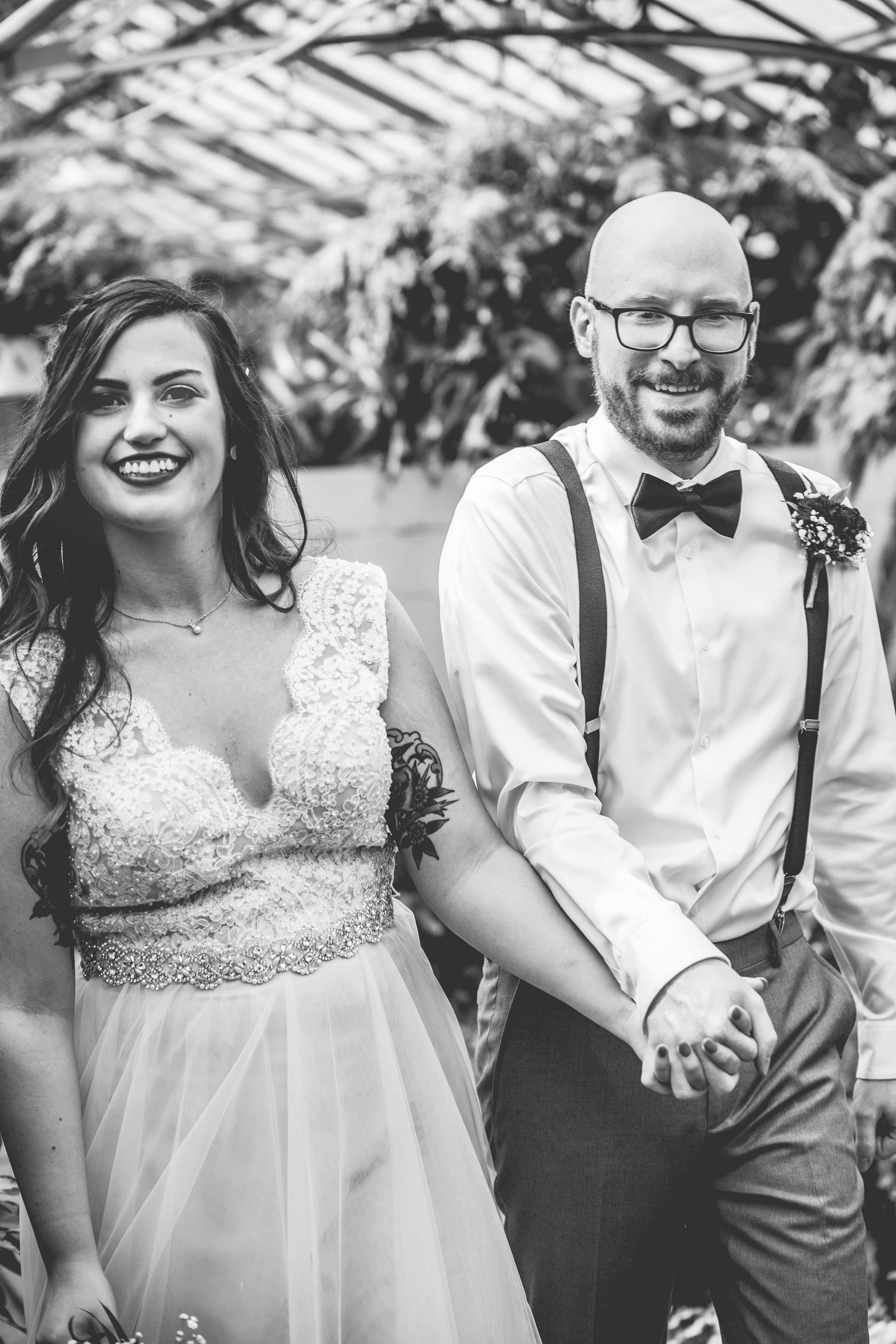 A black and white wedding photo showing a couple in vintage-inspired attire with suspenders and lace.